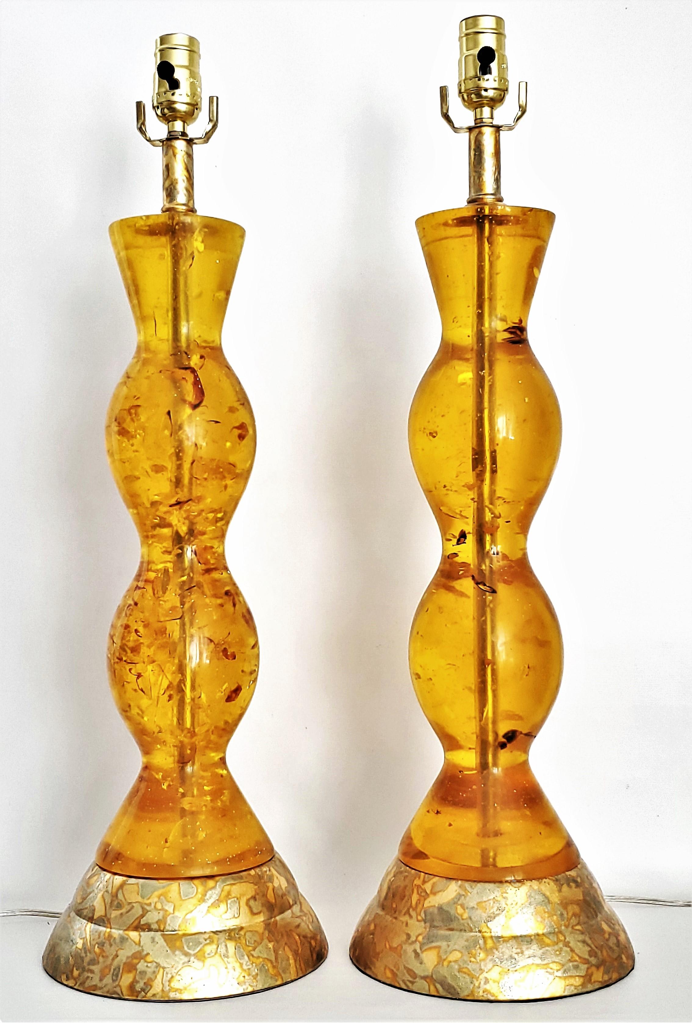 Offering a restored pair of tall amber colored Lucite and gold leafed table lamps, circa 1980.  These are a rare pair of Lucite lamps done in the style of French designer Pierre Giraudon. The Lucite is filled with darker amber colored inclusions