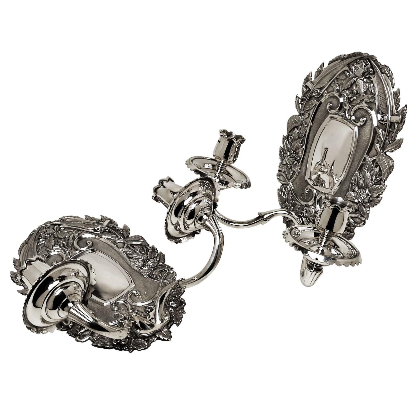 Una magnifica coppia di applique d'epoca Chase & Co. in argento sterling con piastre posteriori ornate e cesellate. I portacandele da parete hanno due rami ciascuno con pozzetti smerlati. Il piatto posteriore presenta bellissimi disegni ornamentali