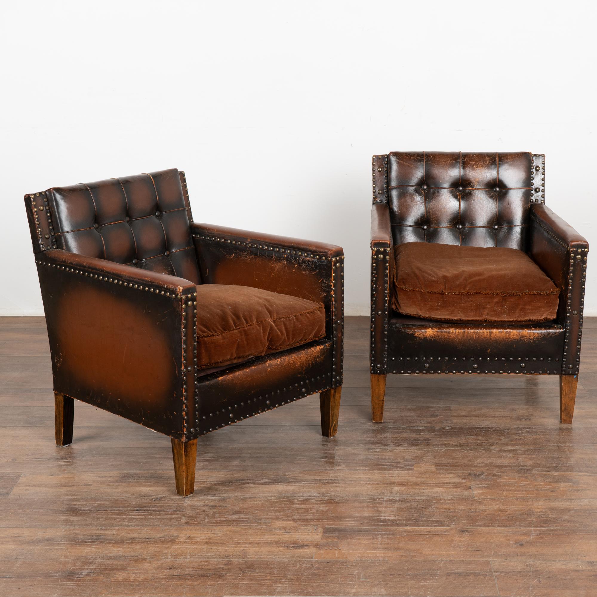 Pair, brown leather arm chairs with crushed velvet cushion seat and elaborate nailhead trim.
Both chairs show extensive age-related crackling, abrasions, scratches, scuffs and signs of wear. Some self-piping worn down to interior cord. Please