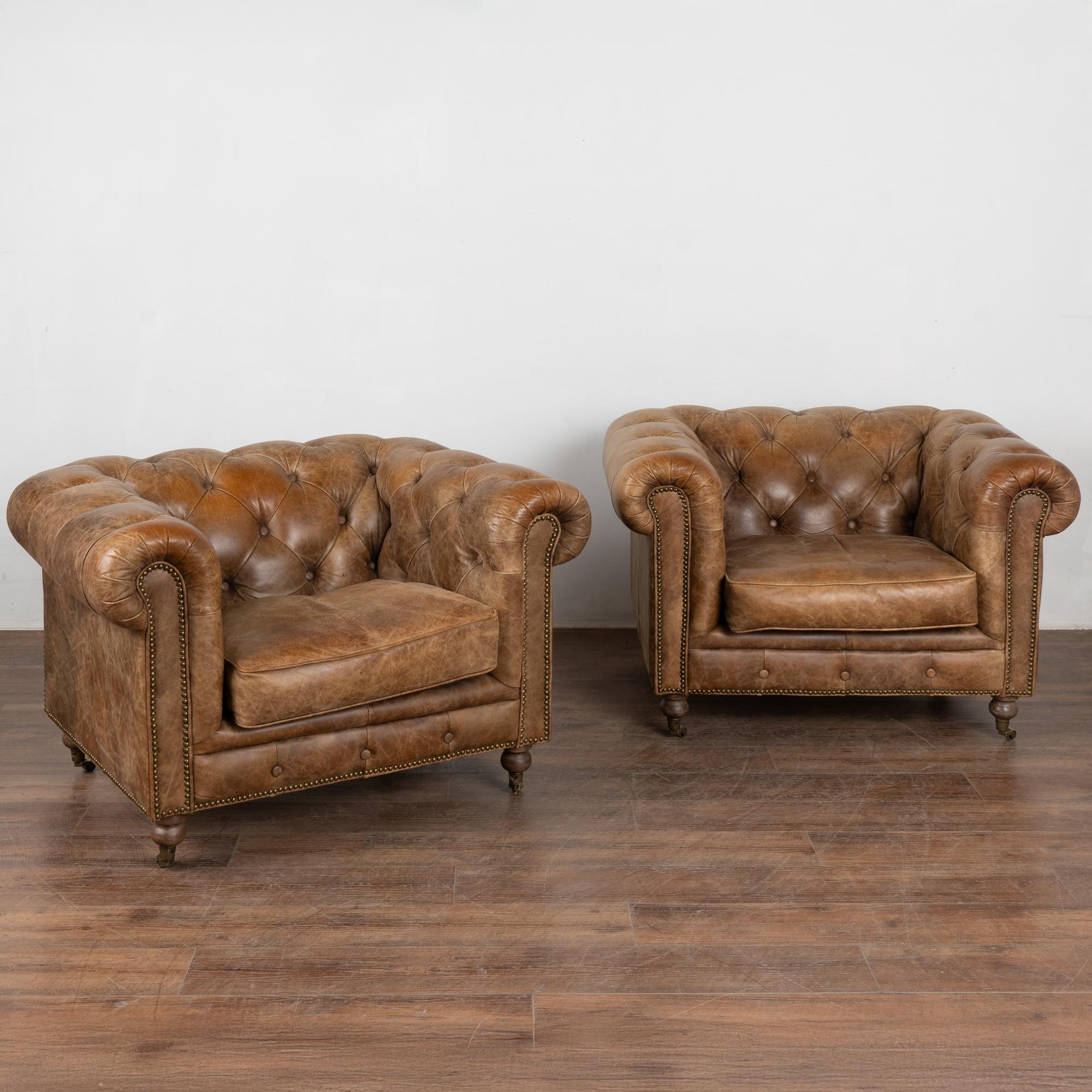 Paire de beaux fauteuils club Chesterfield vintage en cuir marron reposant sur des roulettes.
Rembourré en cuir brun boutonné serré avec garniture de tête de clou, accoudoirs roulés et coussins d'assise lâches avec accès par fermeture