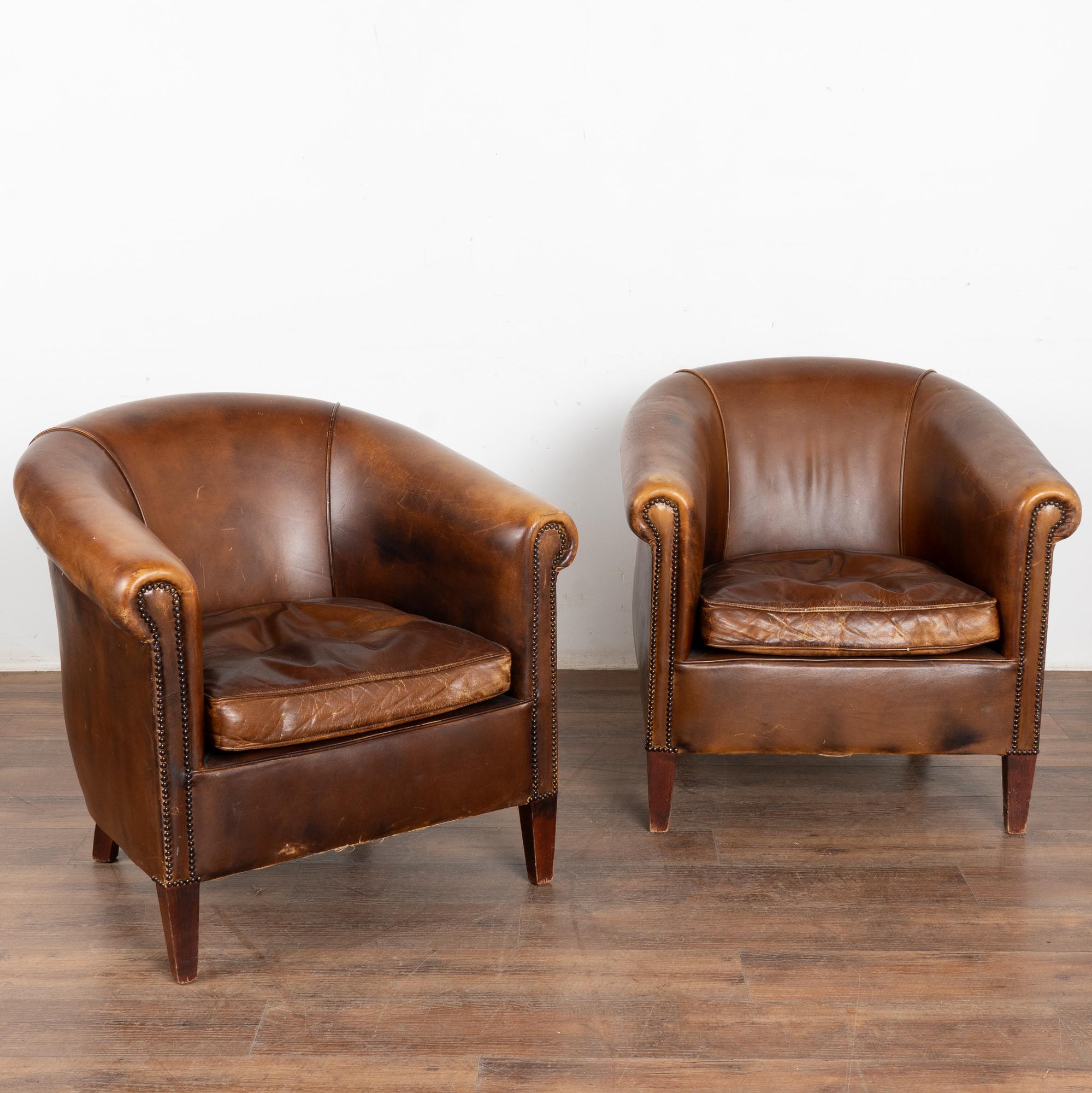 Pair, brown leather tub club chairs with hard wood legs.
Upholstered in vintage brown sheep leather with rich patina, slender rolled arms with nail head trim.
Sold in original vintage condition; solid/stable and sits comfortably snug. Typical age