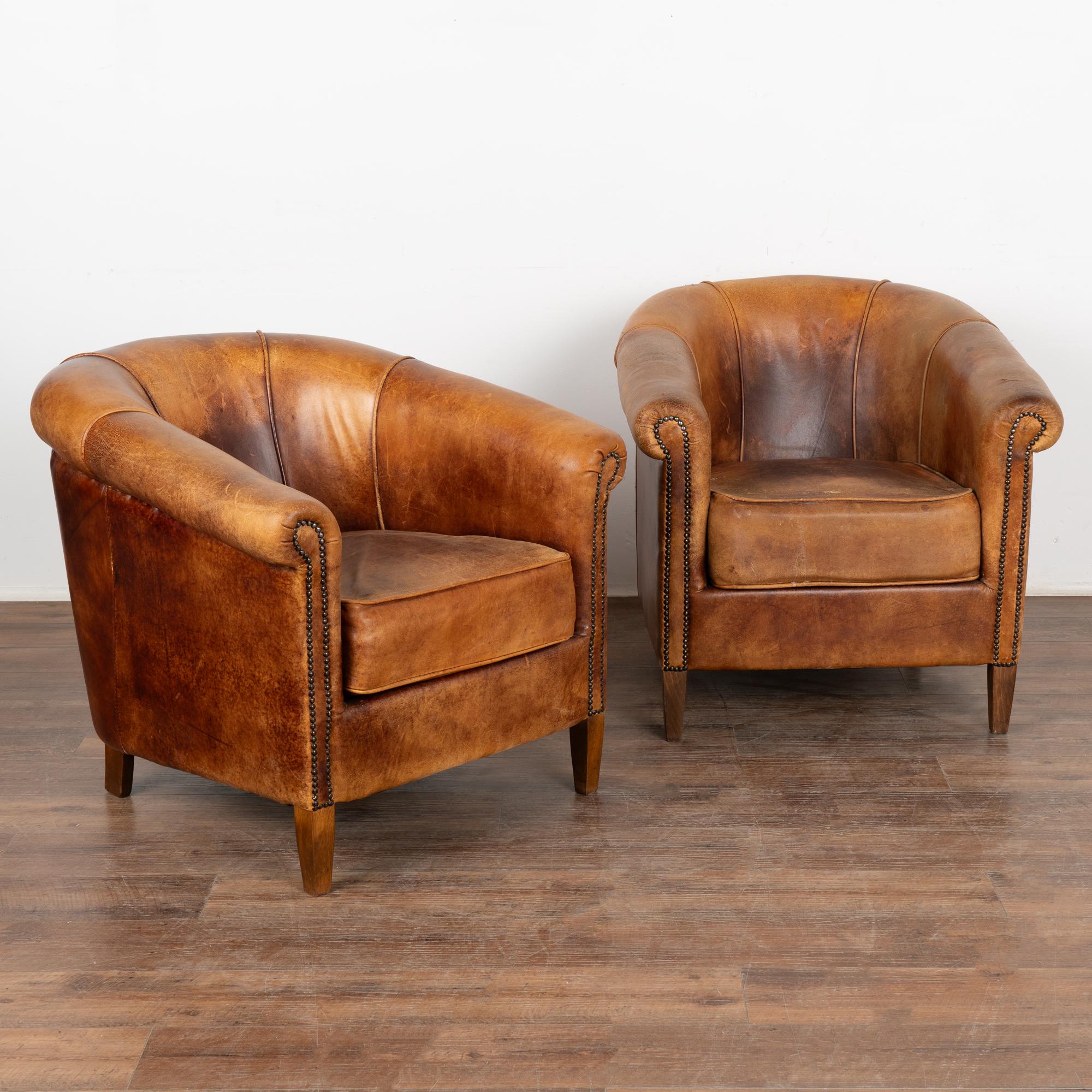 Pair, brown leather tub club chairs with hard wood legs.
Upholstered in vintage brown leather with rich patina, slender rolled arms with nail head trim.
Sold in original vintage condition; solid/stable and sits comfortably snug. Typical age related