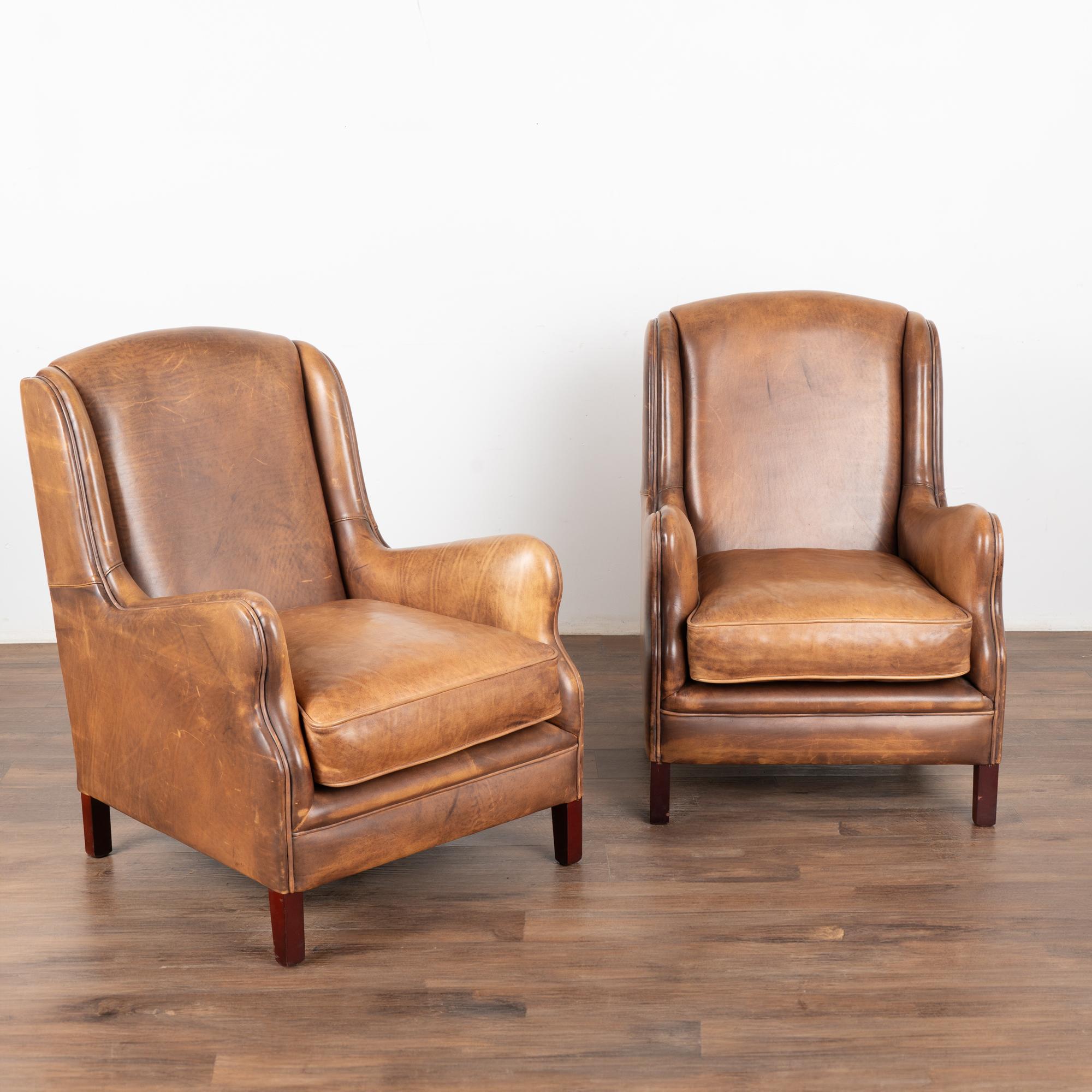 Pair, brown leather arm chairs with hard wood legs. Clean wingback style with stream lined arms and self piping.
Upholstered in smooth vintage brown leather with rich patina.
Sold in original vintage condition; solid/stable and sits