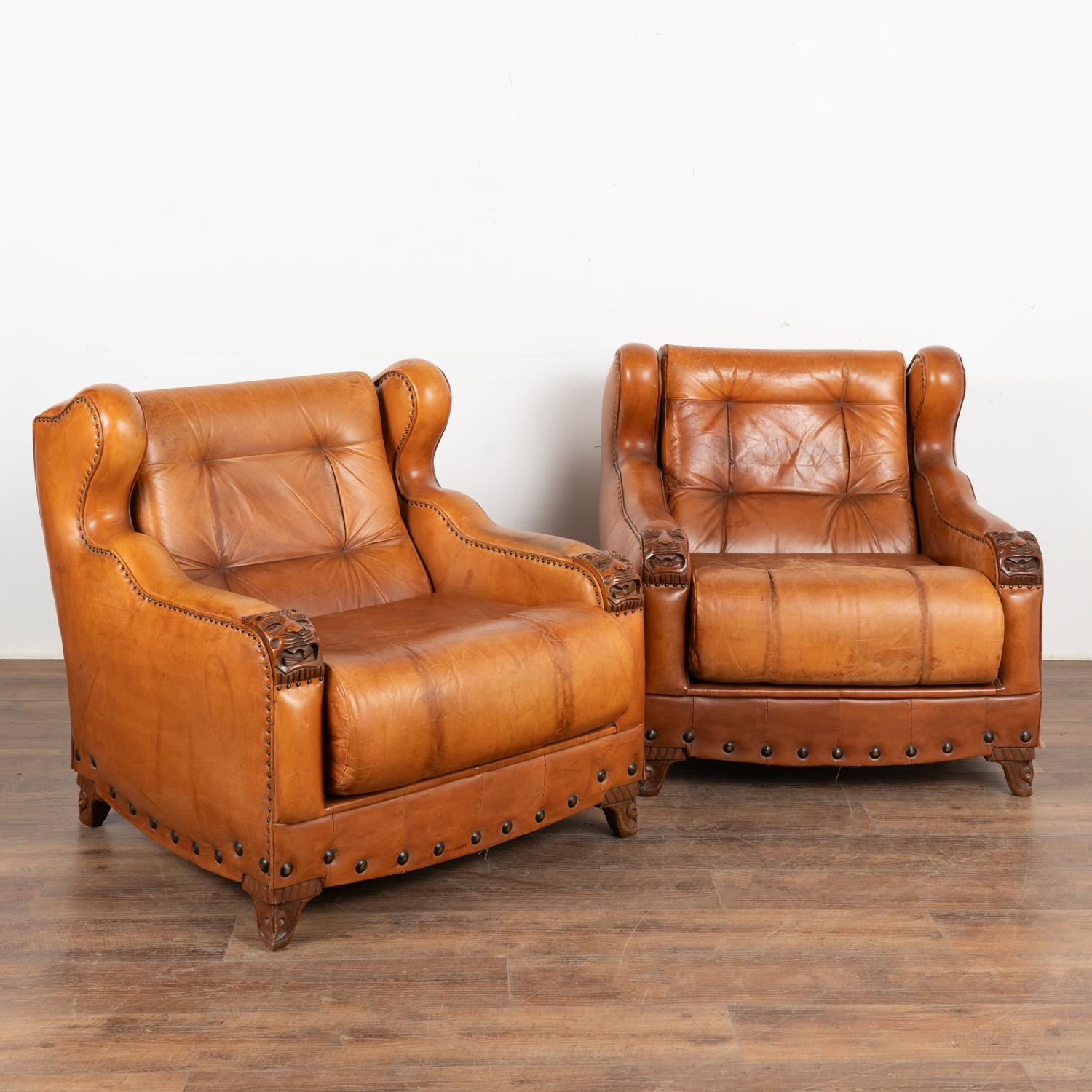 Pair, vintage brown leather wingback armchairs with nail head accents. Faces carved into the arm rests and resting on carved feet.
Sold in original used vintage condition. Signs of wear include discoloration, creasing, stains, scratches,