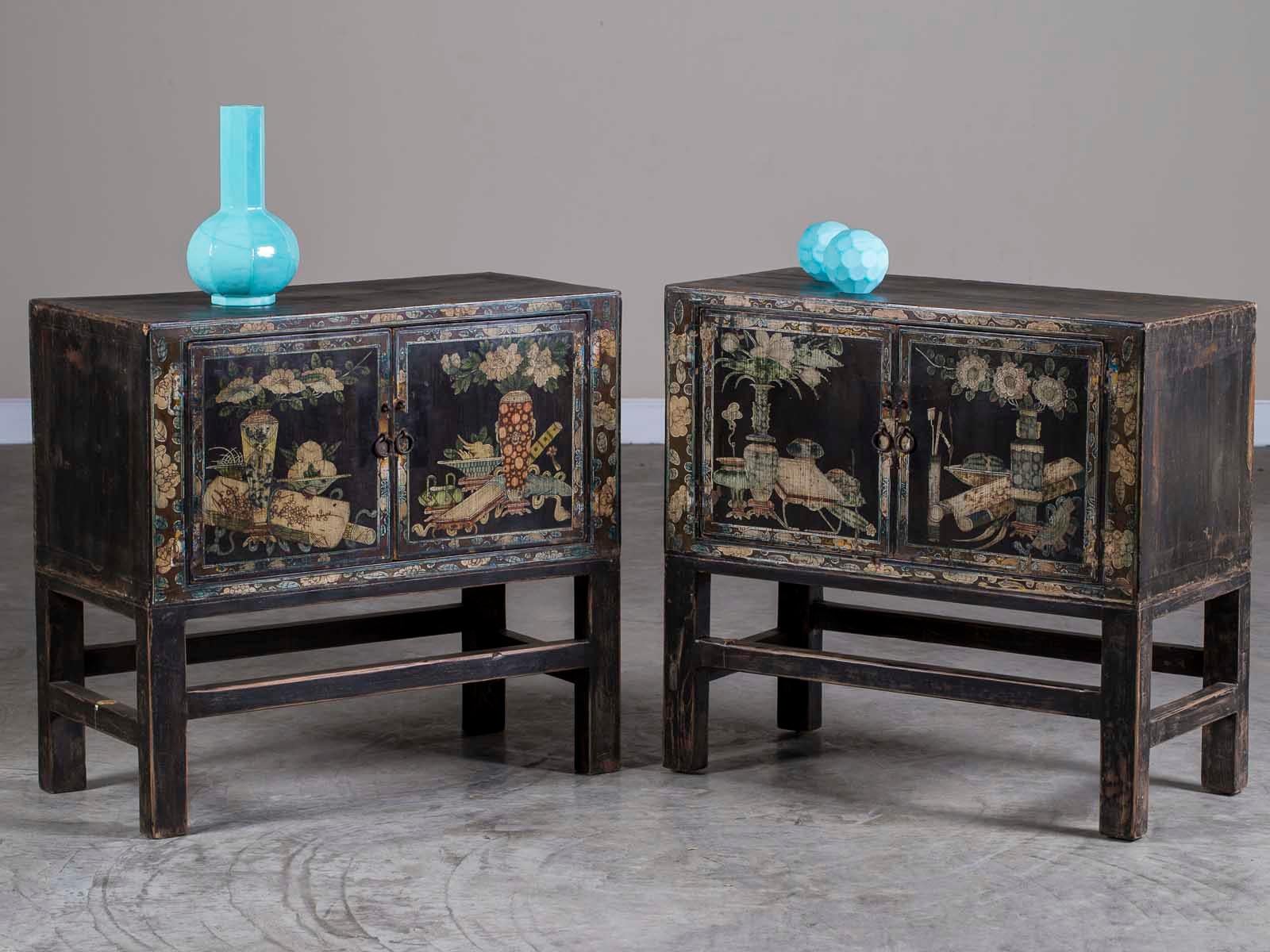 A pair of vintage Chinese painted black lacquer cabinets on stands circa 1940. Please enlarge the photographs to see the hand painted cabinet fronts which each feature a composition of flowers in four different vases as well as scholarly implements