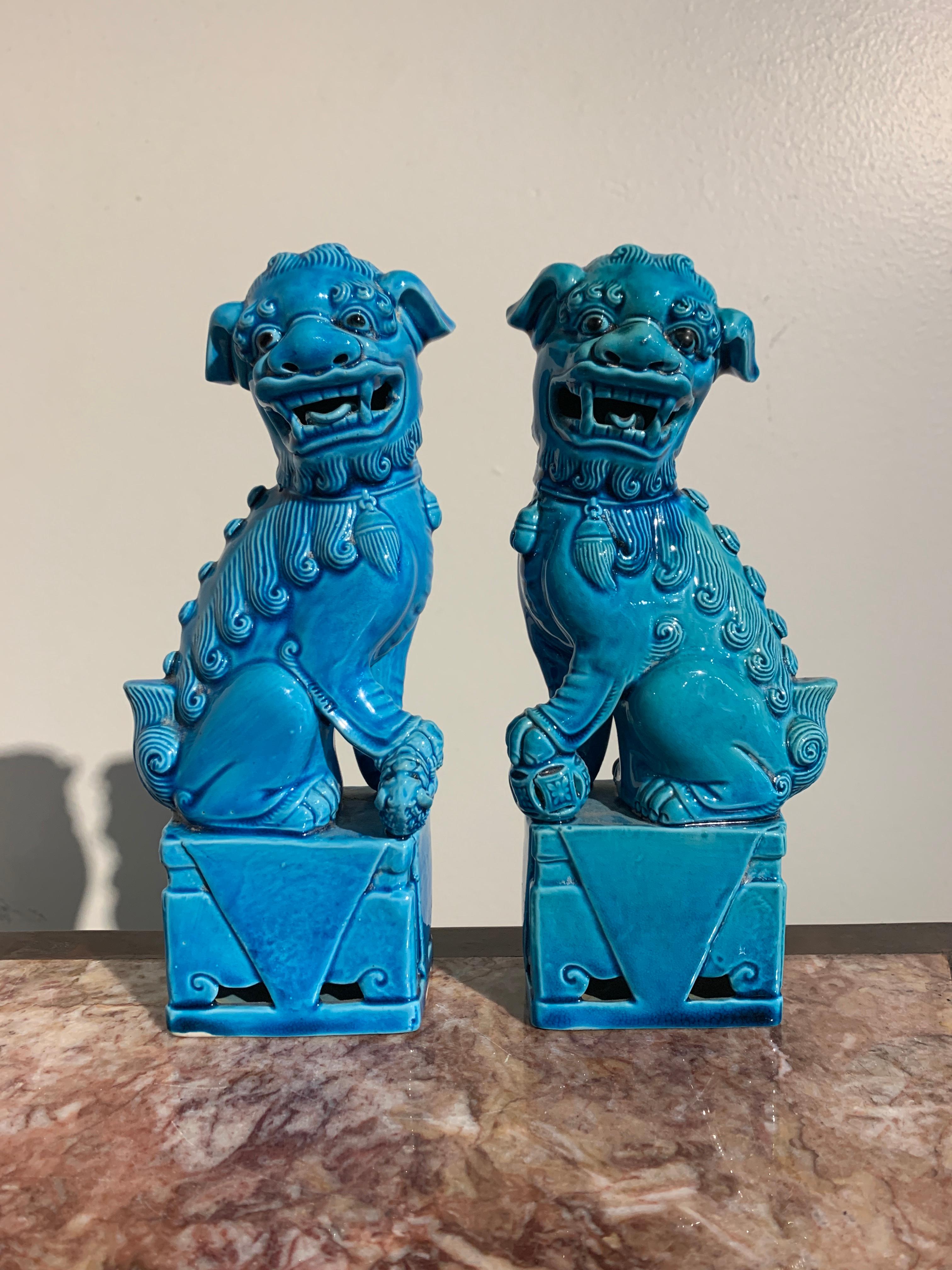 A wonderful small pair of vintage turquoise glazed porcelain foo dogs (also referred to as foo lions), 1970s, Hong Kong.

The charming small pair of foo dogs sit upright on their haunches upon raised pedestals. The male with a ball underfoot, the