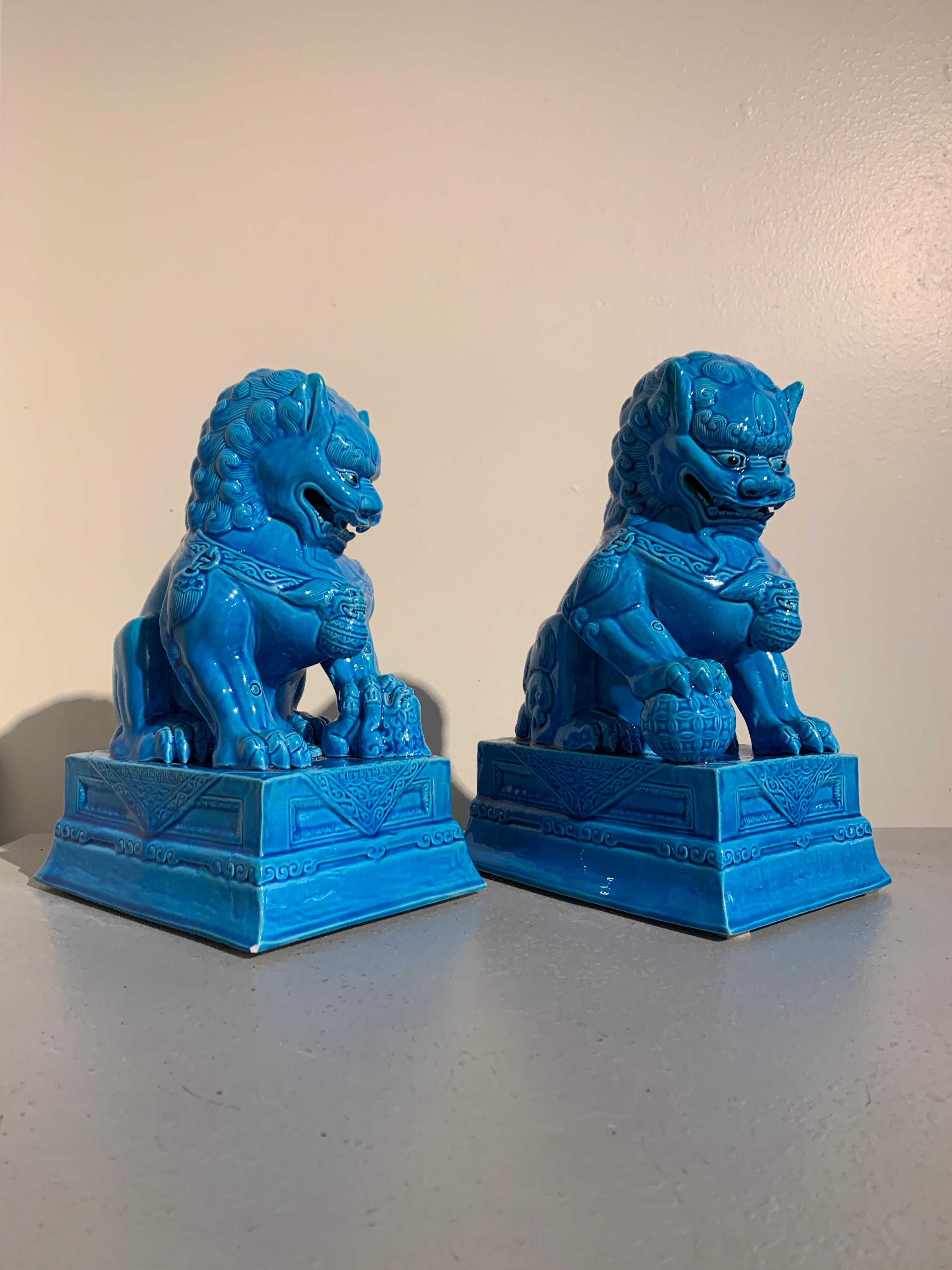 A striking pair of Vintage Chinese turquoise glazed porcelain foo dogs or guardian lions, circa 1980s. 

The pair of lions, modeled after the pair of Ming Dynasty carved stone lions that guard the Forbidden City in Beijing, sit upon their haunches