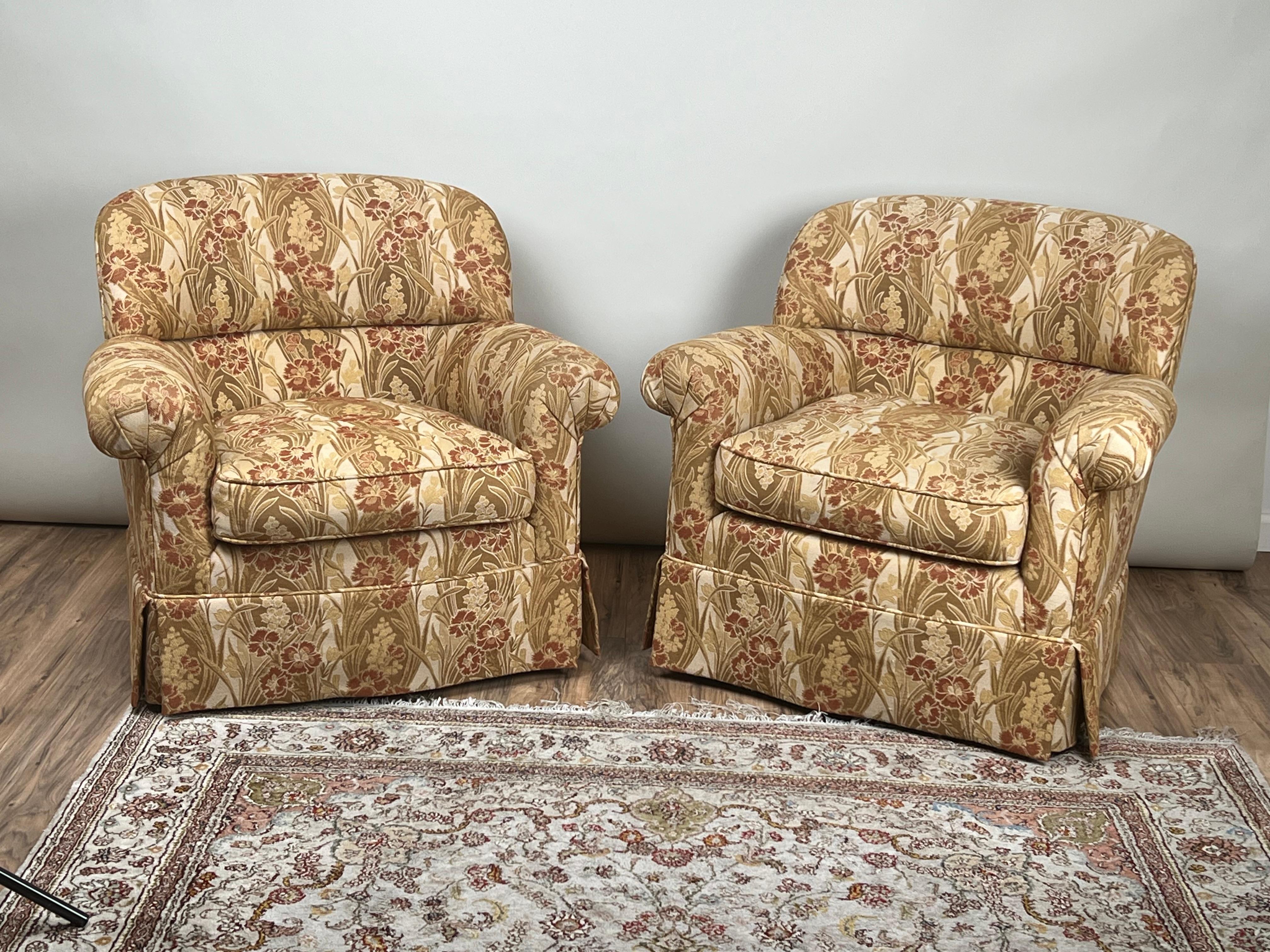 This pair of vintage custom upholstered club chairs offers both comfort and versatility, with one chair designed as a stationary piece and the other incorporating a smooth swivel base. Upholstered in a richly patterned fabric with floral and foliate