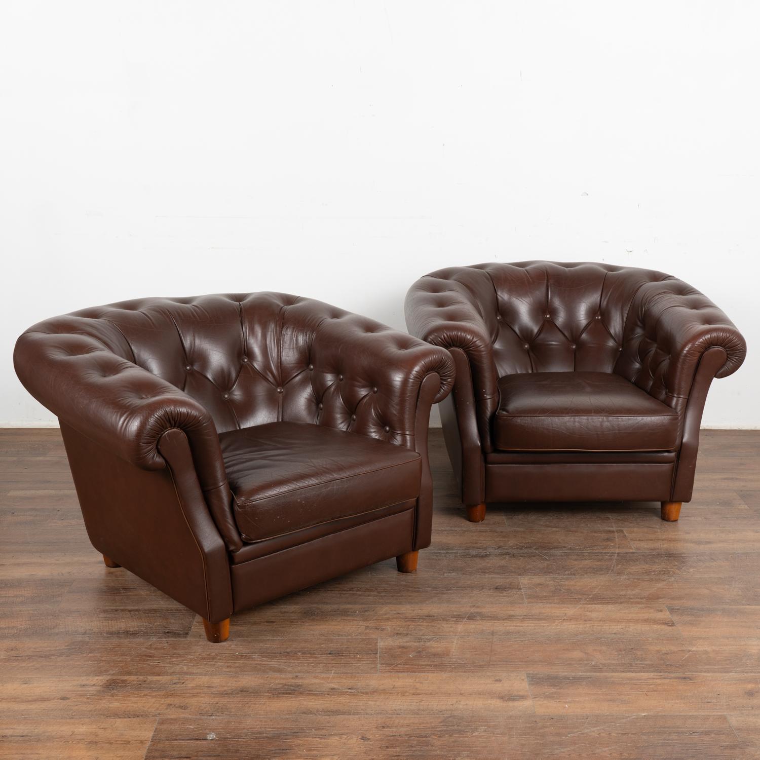 This pair of vintage leather club chairs are welcoming with barrel shaped arms and tufted backs with self covered buttons and piping.
This pair shows signs of typical age and wear to the dark brown leather including scratches, stains, scuffs,