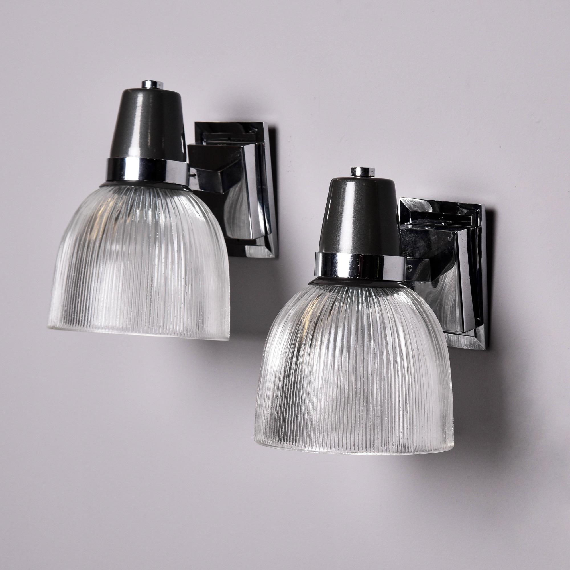 Found in England, this pair of industrial style sconces date from the late 1970s. Each light has a rectangular chrome backplate, chrome and black fittings and clear, ridged glass shades. Each has a single socket that has been rewired for US