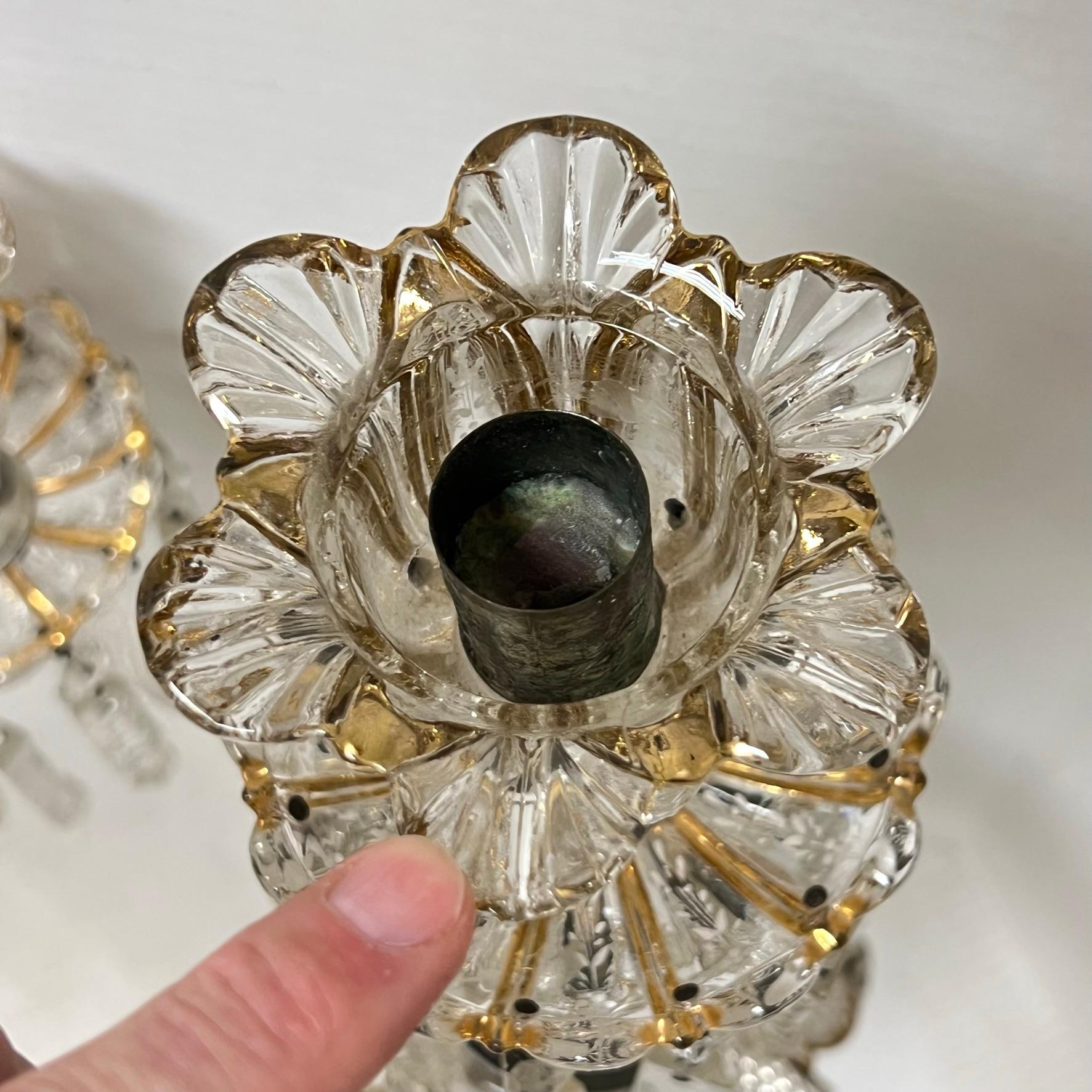 Pair of vintage molded glass candelabra in the Baccarat style with white floral painted and gilt accents and numerous cut crystal pendants.  One with old lead repairs to one arm, one missing crystal pendant, repair or replacement of glass below the