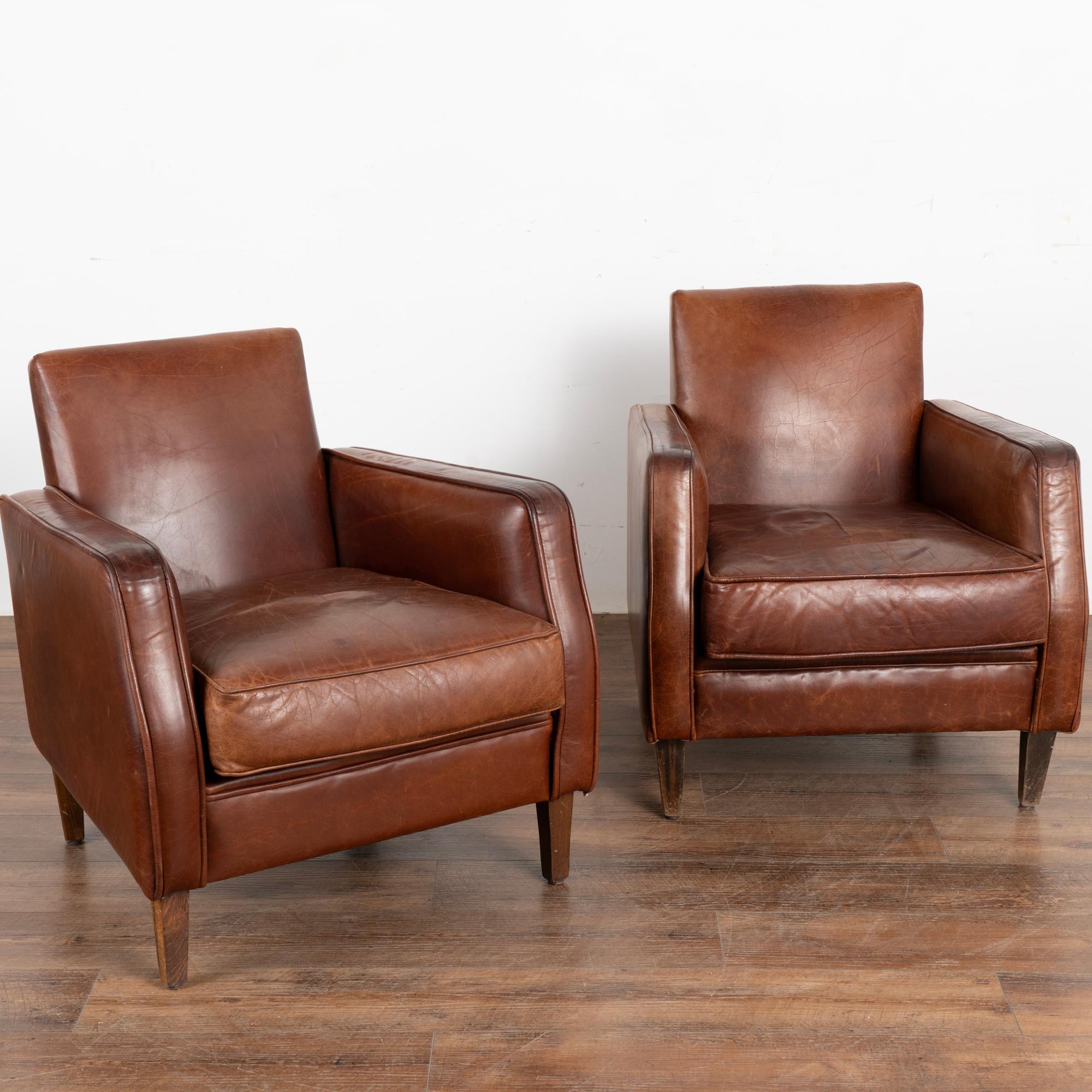Pair, brown leather club arm chairs with hard wood legs.
Upholstered in vintage brown leather with rich patina and streamlined arms, decorative nail heads along back.
Sold in original vintage condition; solid/stable and sits comfortably. Typical age