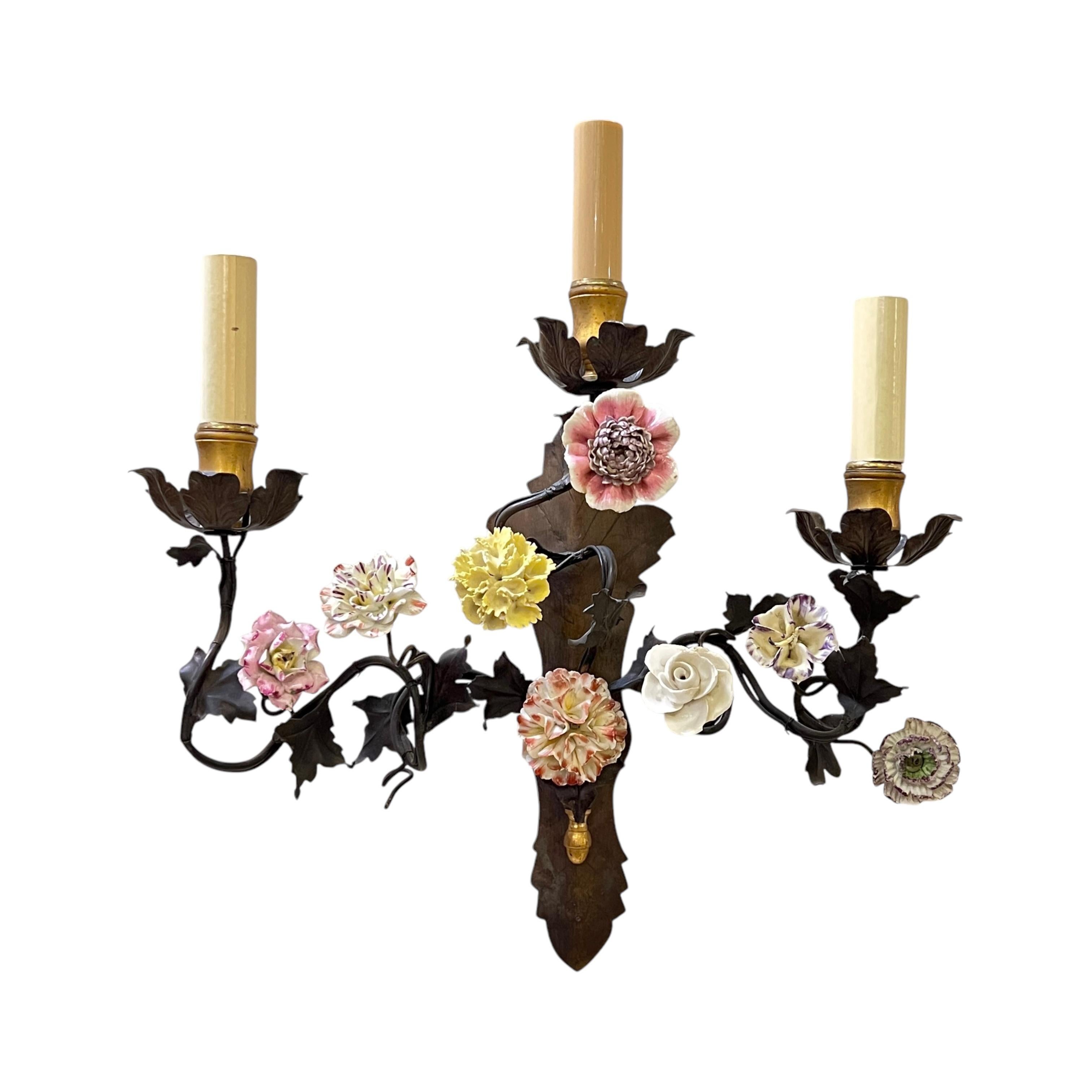Pair of vintage sconces, circa 1940s, finely crafted from patinated metal and brass with numerous finely glazed and colorful porcelain flower heads.  16 by 13 1/2 by 5 1/2 and 15 by 14 by 4 inches respectively.  Each with modern candelabra size