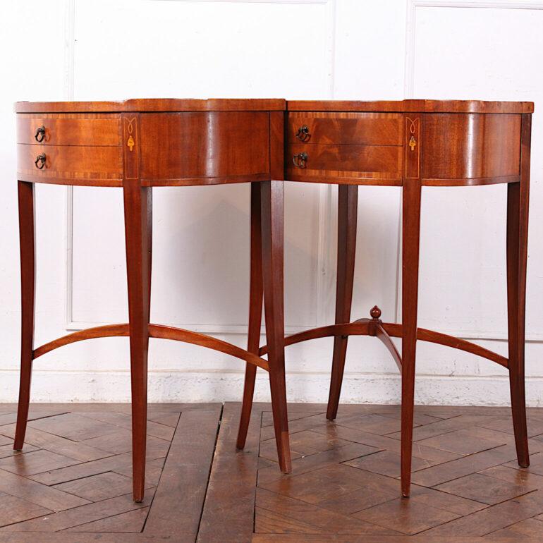 A pair of vintage Sheraton style oval side tables or nightstands, each with a single banded flame mahogany drawer and raised on elegant tapering splayed legs with 'X' stretcher. Tops with inset gilt tooled leather surface.