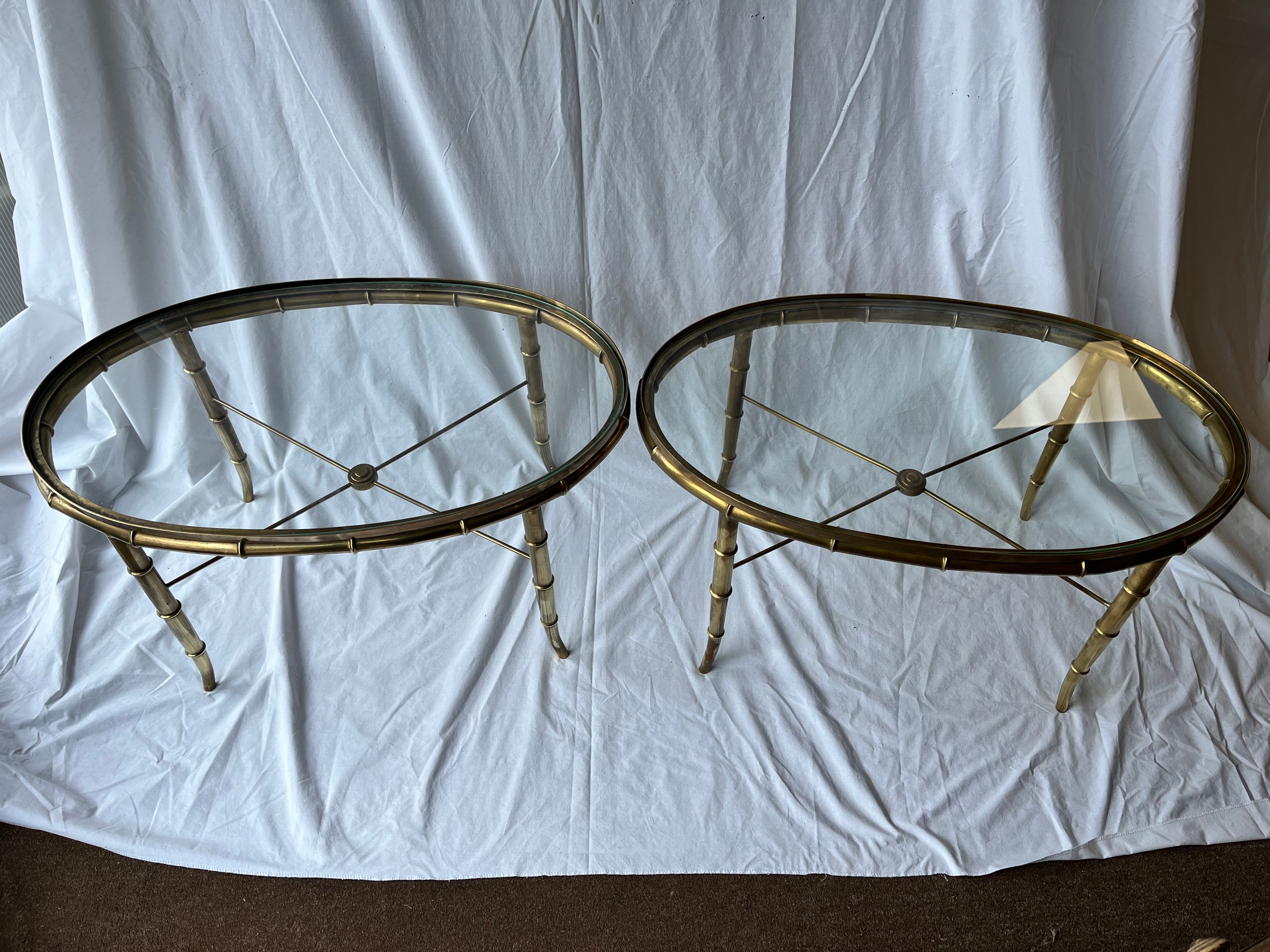 A vintage circa 1980's (but possibly earlier) pair of Italian faux bamboo brass tables with inset glass tops. The oval form has a lip that accepts the glass top. The tubular, faux bamboo structure sits just below the lip. The four tapered tubular,