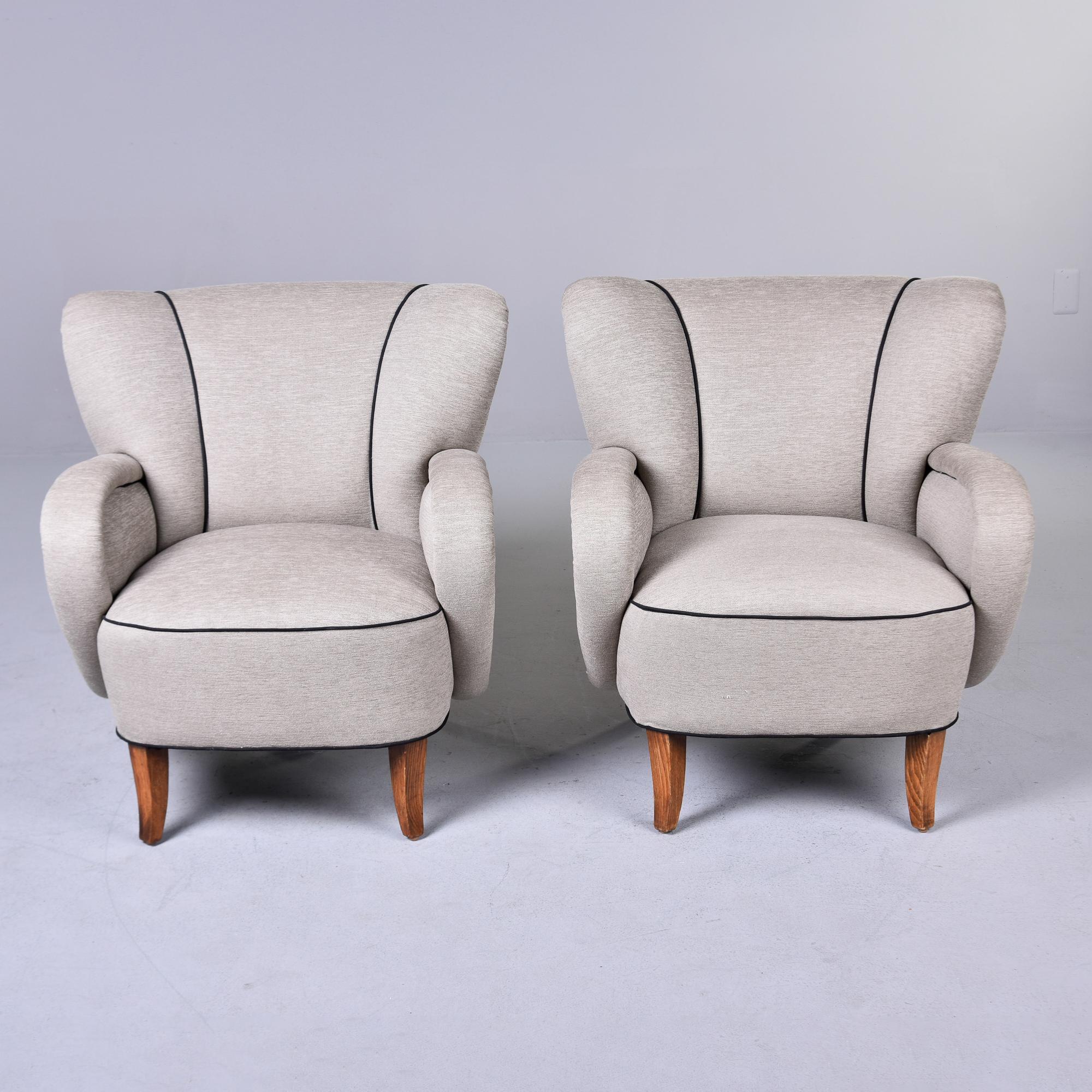 Found in Italy, this pair of Italian arm chairs date from the late 1940s / early 1950s. These chairs have been newly upholstered in a greige fabric with contrasting black welting that highlights the curves. Unknown maker. Sold and priced as a pair.