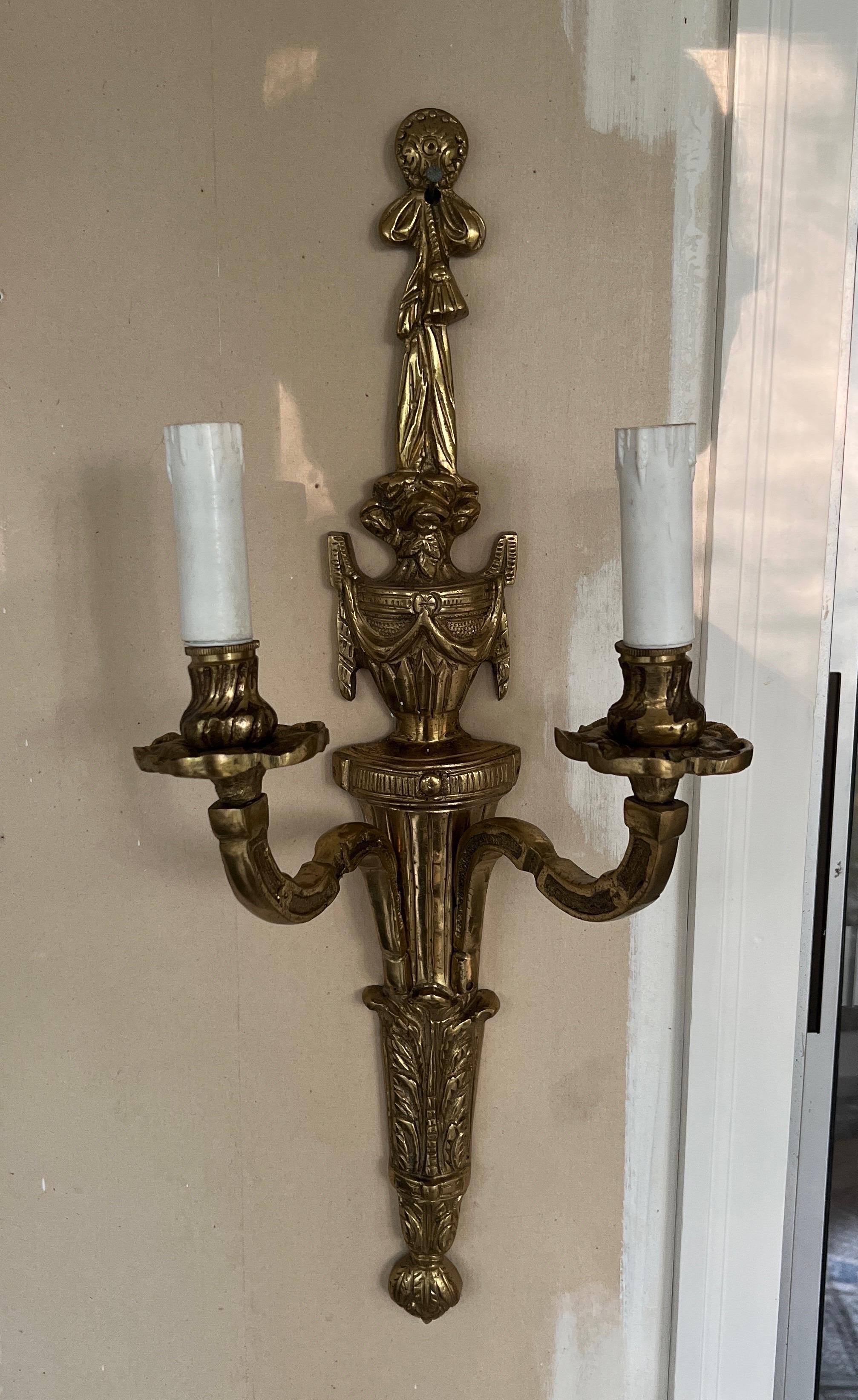Italian, 20th century. 

A pair of gilt bronze wall sconces with traditional urn form body, draped rope header and two arms with faux wax candle covers. Marked to verso 