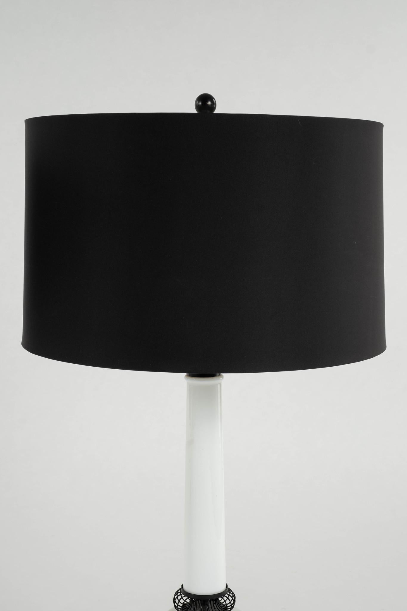 Illuminate your space with this contemporary pair of vintage milk glass table lamps. These lamps exude timeless design and sophistication, featuring sleek white milk glass, black enameled metal accents and black shades. 