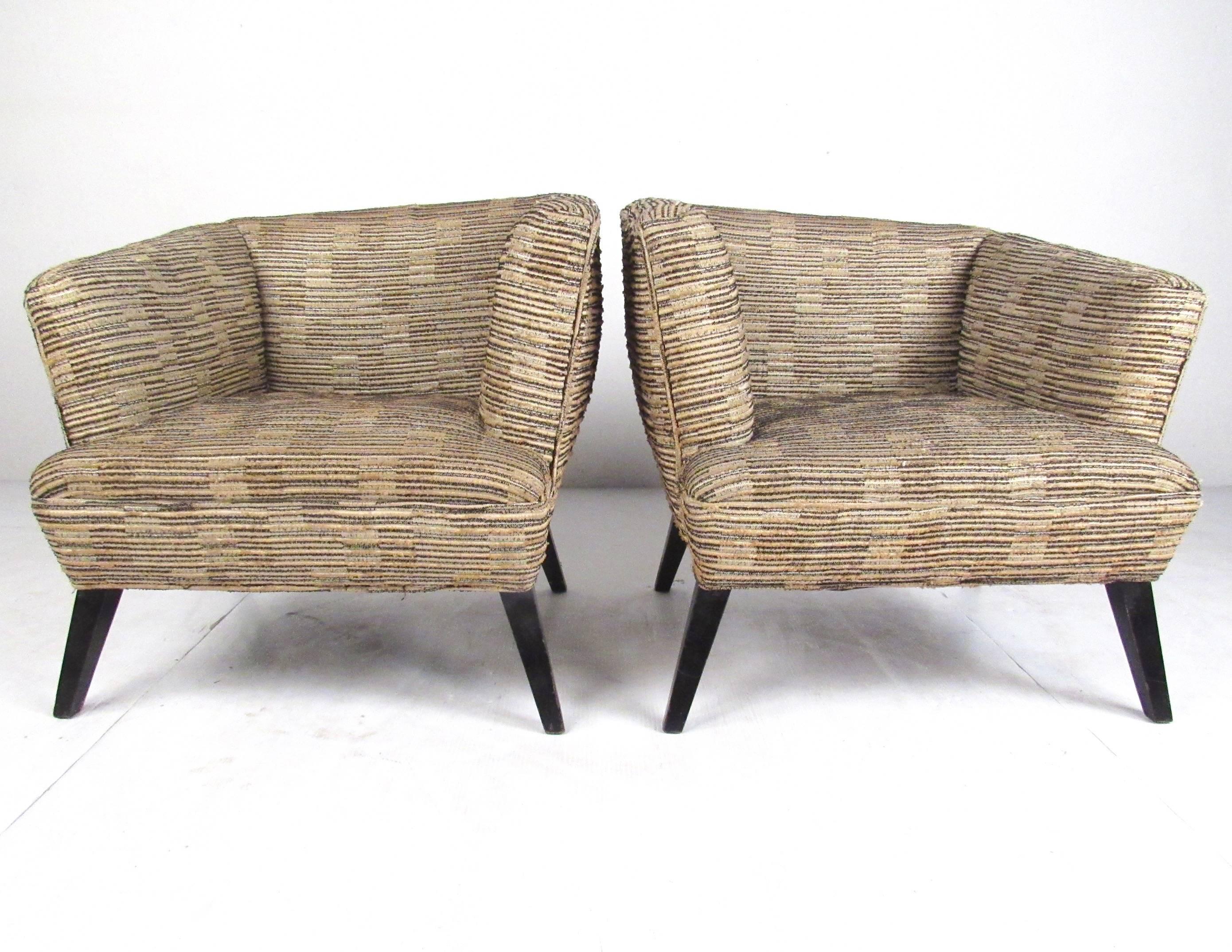 This unique pair of matched lounge chairs features plush upholstered club seats with abstract angled seat backs for an Art Deco like appeal. Mid-Century Modern design is showcased in the vintage fabric, original modern lines, and tapered hardwood