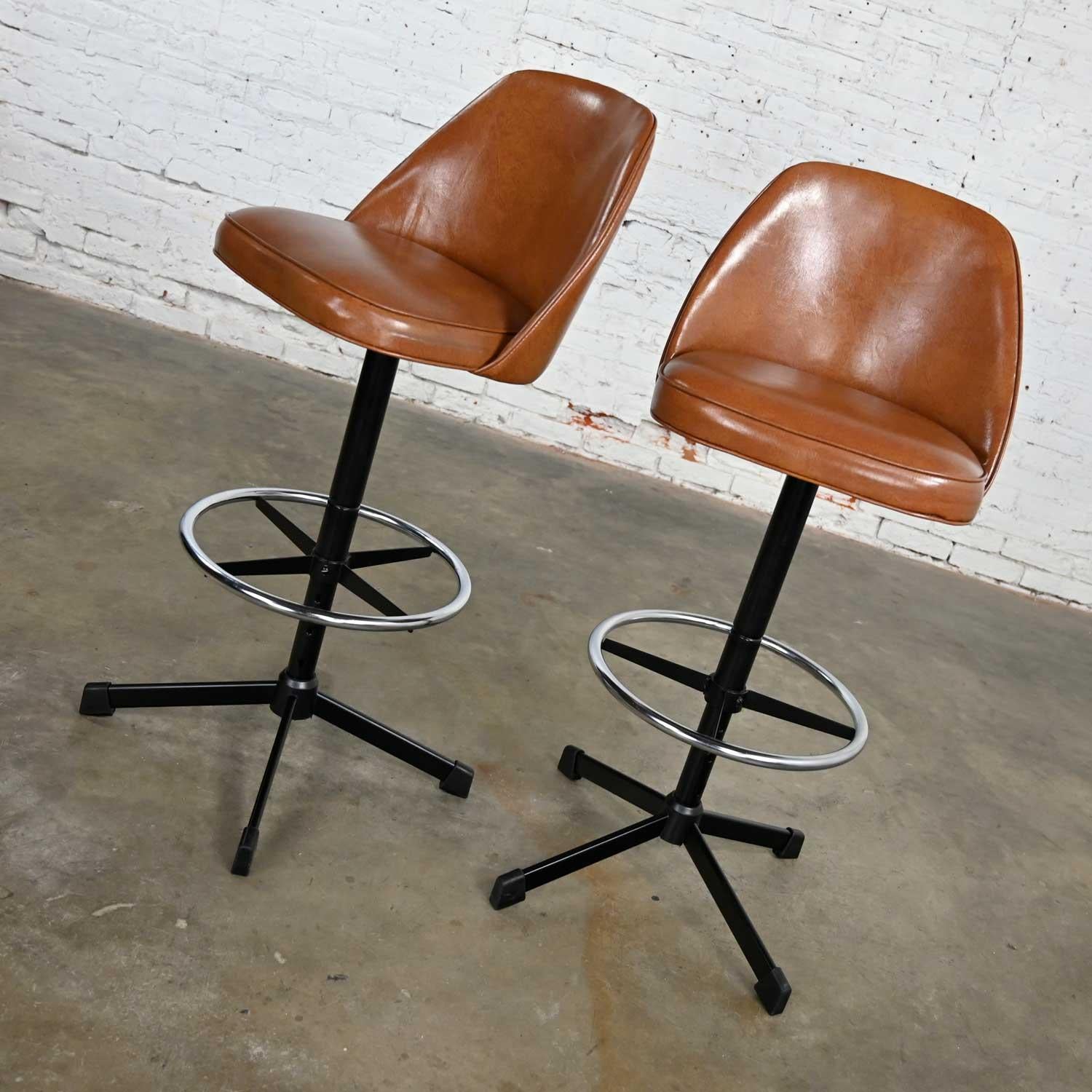 Lovely pair of vintage modern Cosco counter or bar stools comprised of cognac, aka brown, vinyl, black painted steel shafts, 4 prong bases, chrome ring footrests, swivel option, and 4 height adjustments. Beautiful condition, keeping in mind that