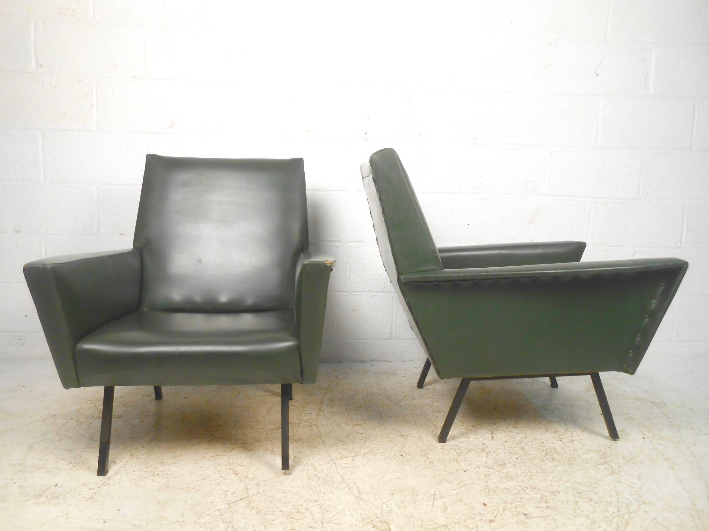 This stylish pair of midcentury lounge chairs feature vintage Danish modern design and include sturdy metal legs, winged arm rests, and high back seats upholstered in vinyl. Elegant and statuesque pair of high back Scandinavian style lounge chairs