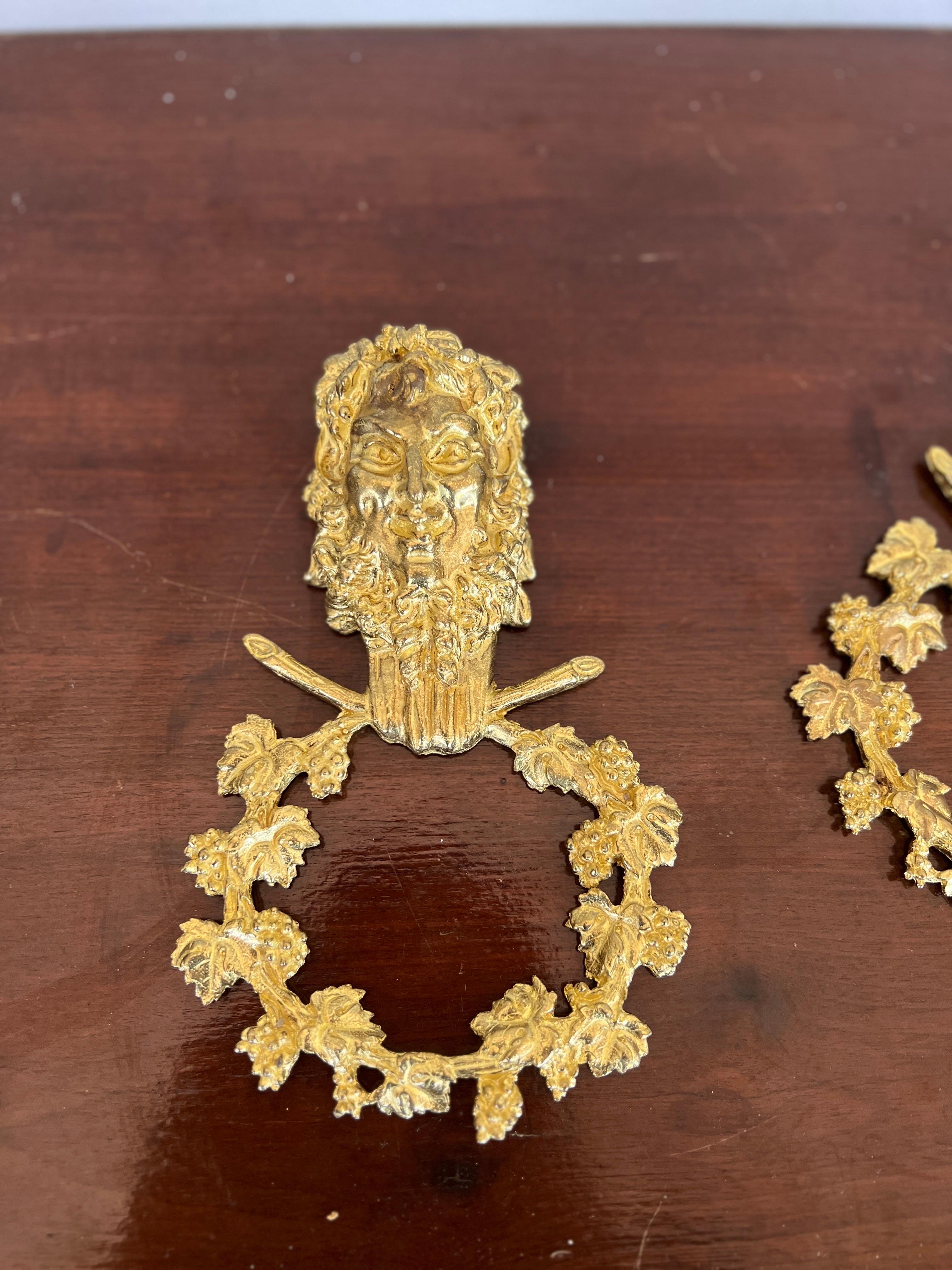 Likely French, mid 20th century.

A pair of gilt bronze wall accents in the Neoclassical taste. Each depicting a Satyr face above a laurel wreath. Hanger to verso. Unmarked.