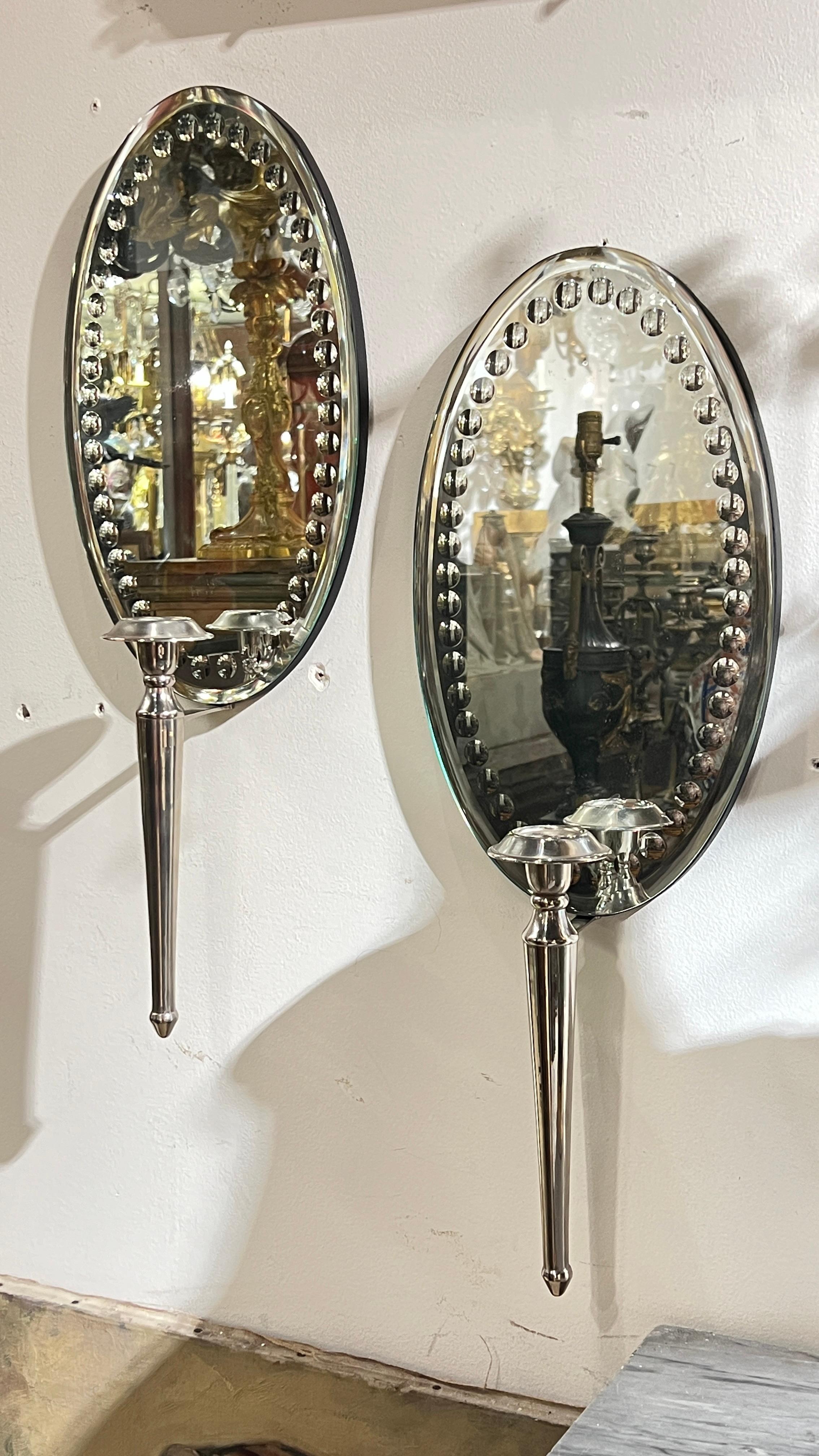 Pair of mid-century modern period mirror-back wall lights with oval shaped mirrored wall plates decorated with engraved circular dot boarder.  21 by 8 by 4 inches.  Not wired.
