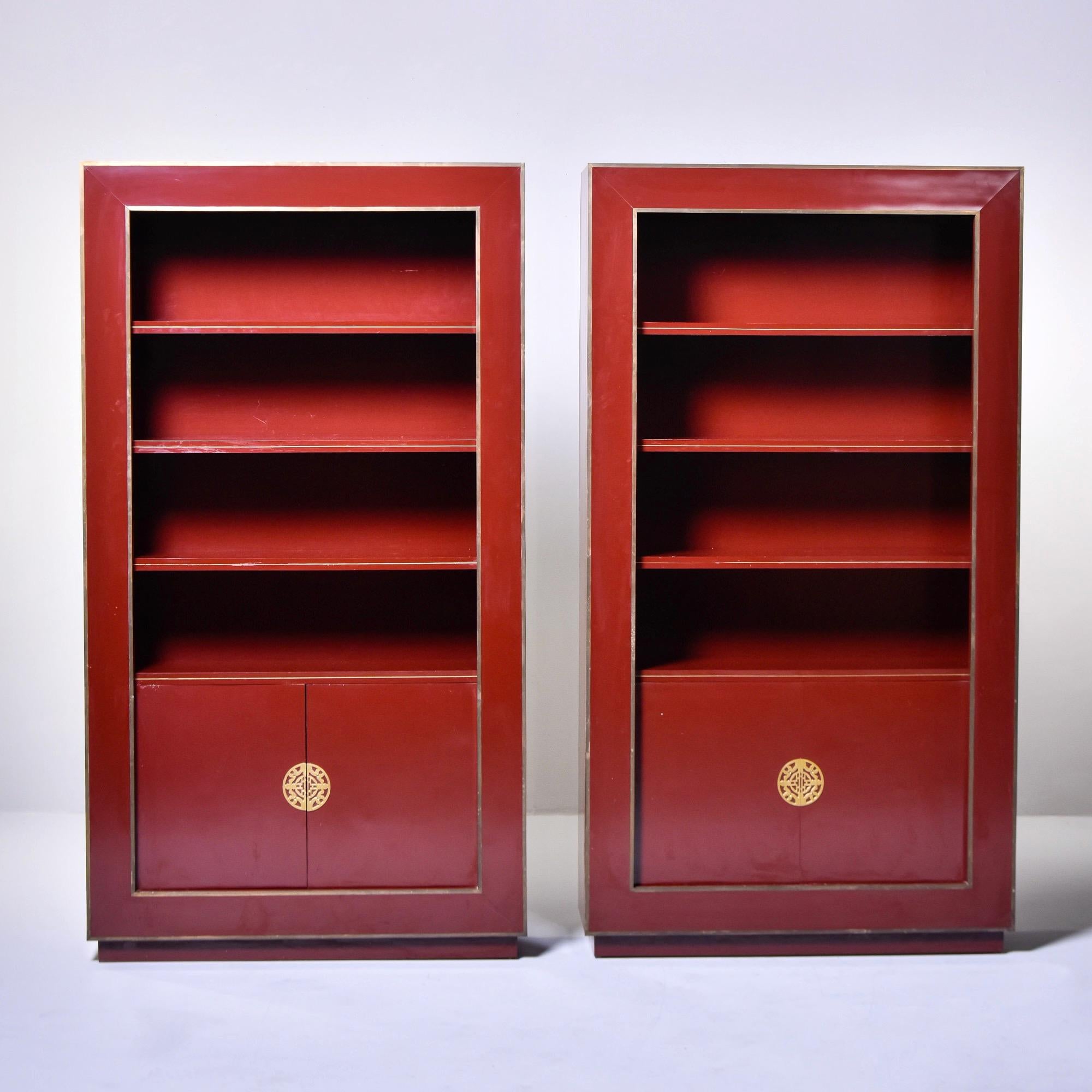 Found in Europe, this pair of Chinoiserie style shelf cabinets date from the 1970s. These are in a dark, ox blood red lacquer with brass trim and hardware. Each cabinet has three adjustable shelves on the top section and one adjustable shelf behind