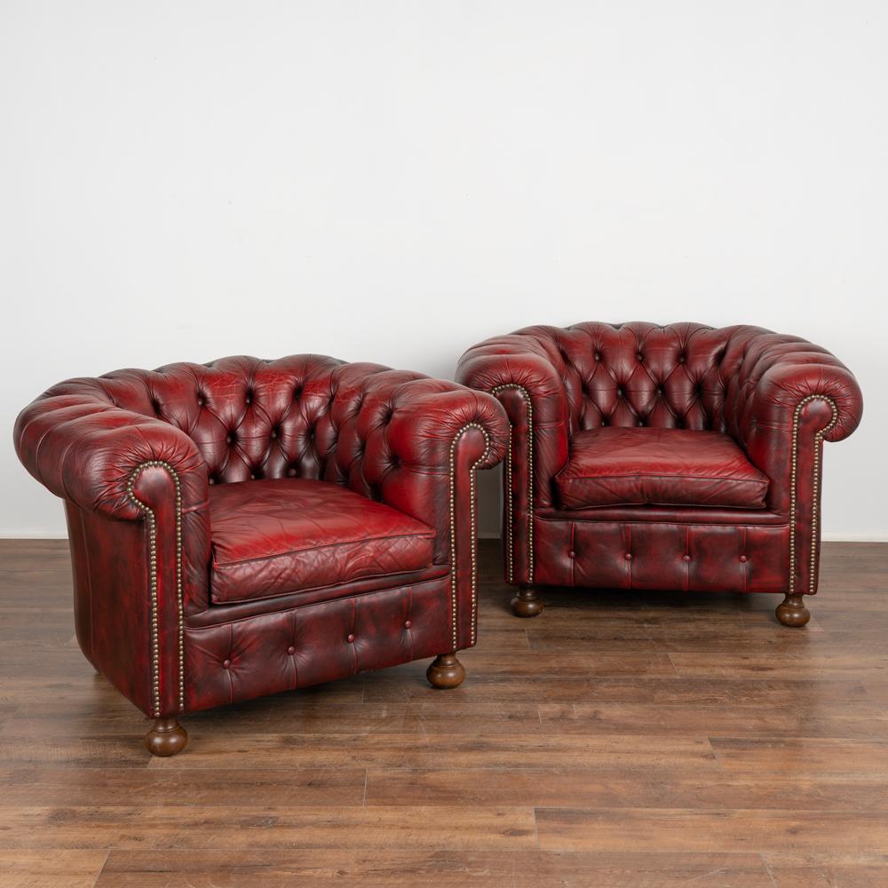 Pair, vintage red leather chesterfield style club armchairs.
Upholstered in studded, button-tufted red leather, rolled arms and loose seat cushions.
Sits comfortably; sold in original vintage condition. Wear, scuffs, scratches, creases,