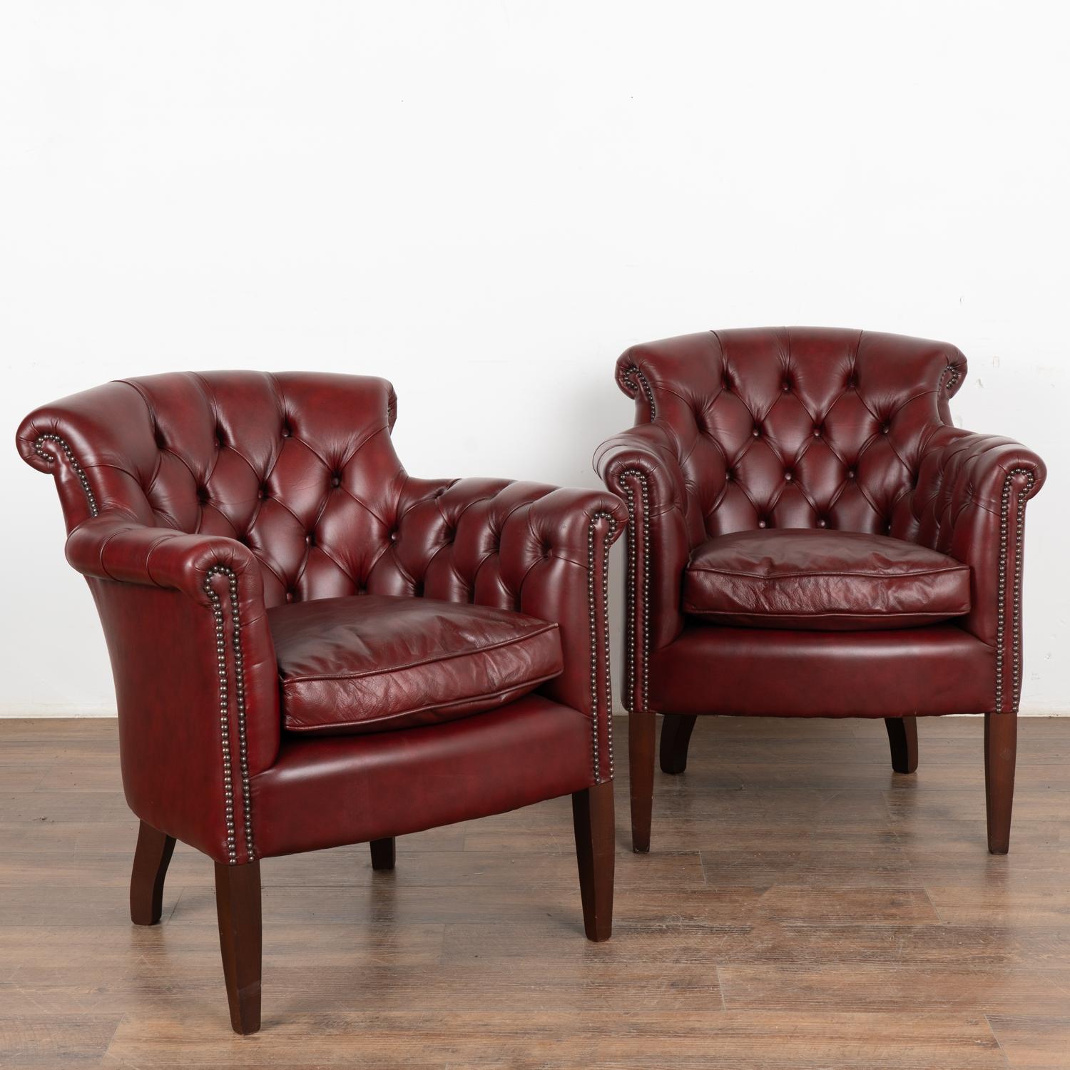 Handsome pair of red leather Chesterfield style arm chairs with tufted/buttoned back and narrow rolled arms with nailhead trim.
Vintage leather reflects years of use including scuffs, scratches, impressions, crackling, etc. Buttons in place.
Sold in
