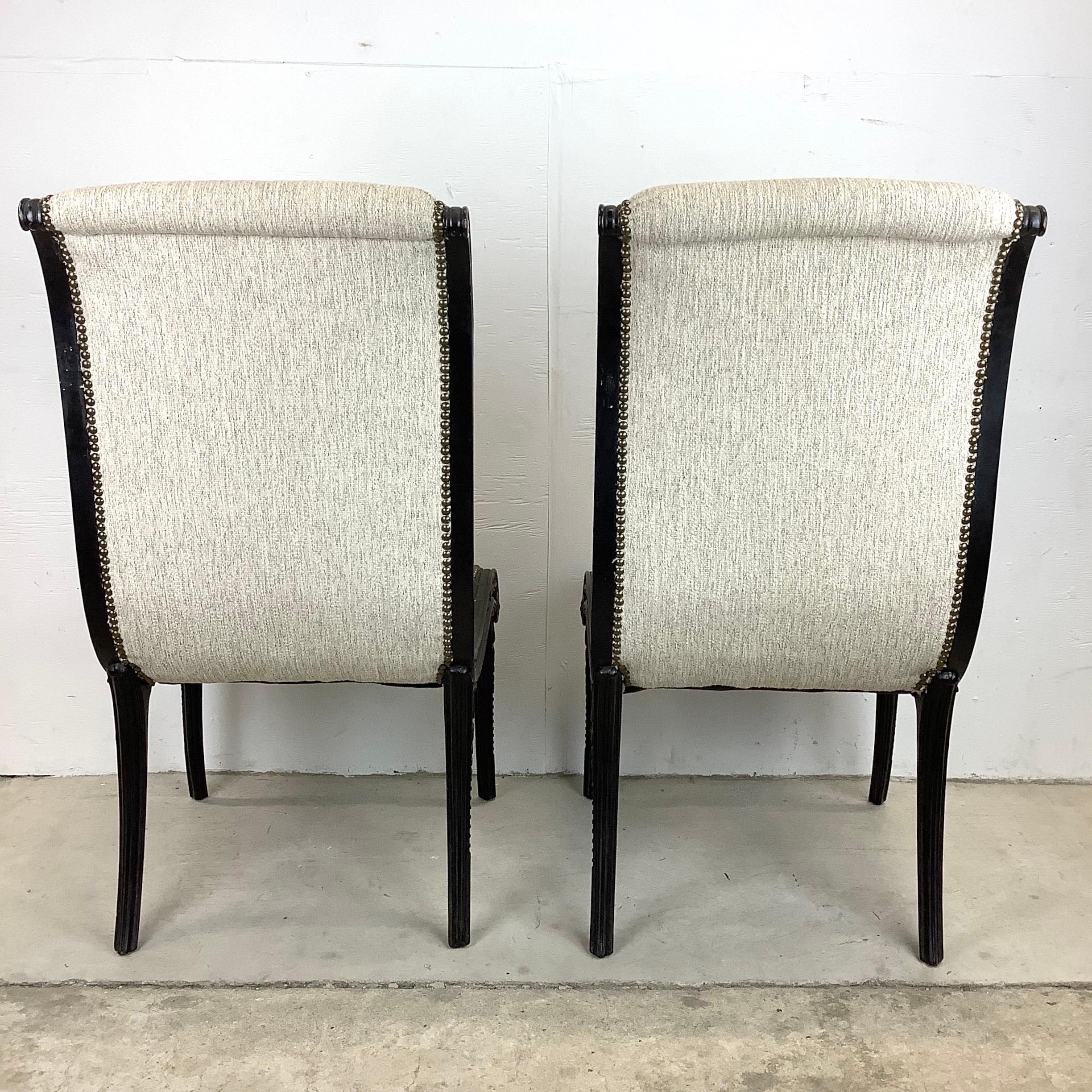 This stunning pair of high back regency modern slipper chairs feature ornate ebonized wooden frames with gilt detail and brass studded trim. The comfortably padded upholstered seats make this an excellent set of occasional chairs perfect for salon