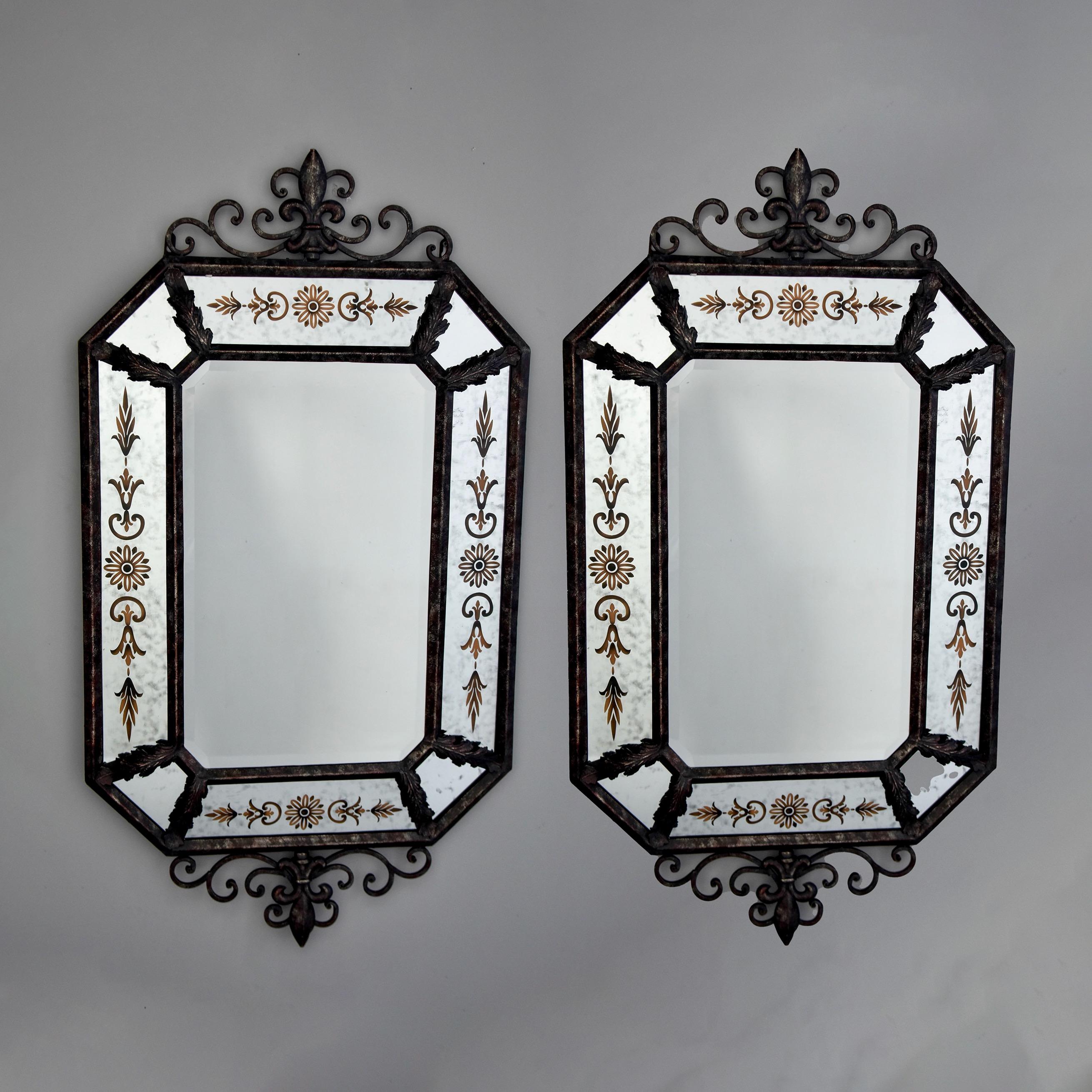 This pair of Spanish iron framed mirrors date from the 1990s. Dark iron and metal framed mirrors feature scrolled, decorative crests and finials along with acanthus leaf decorations. Outer frame of eight mirrored and painted panels surrounds a