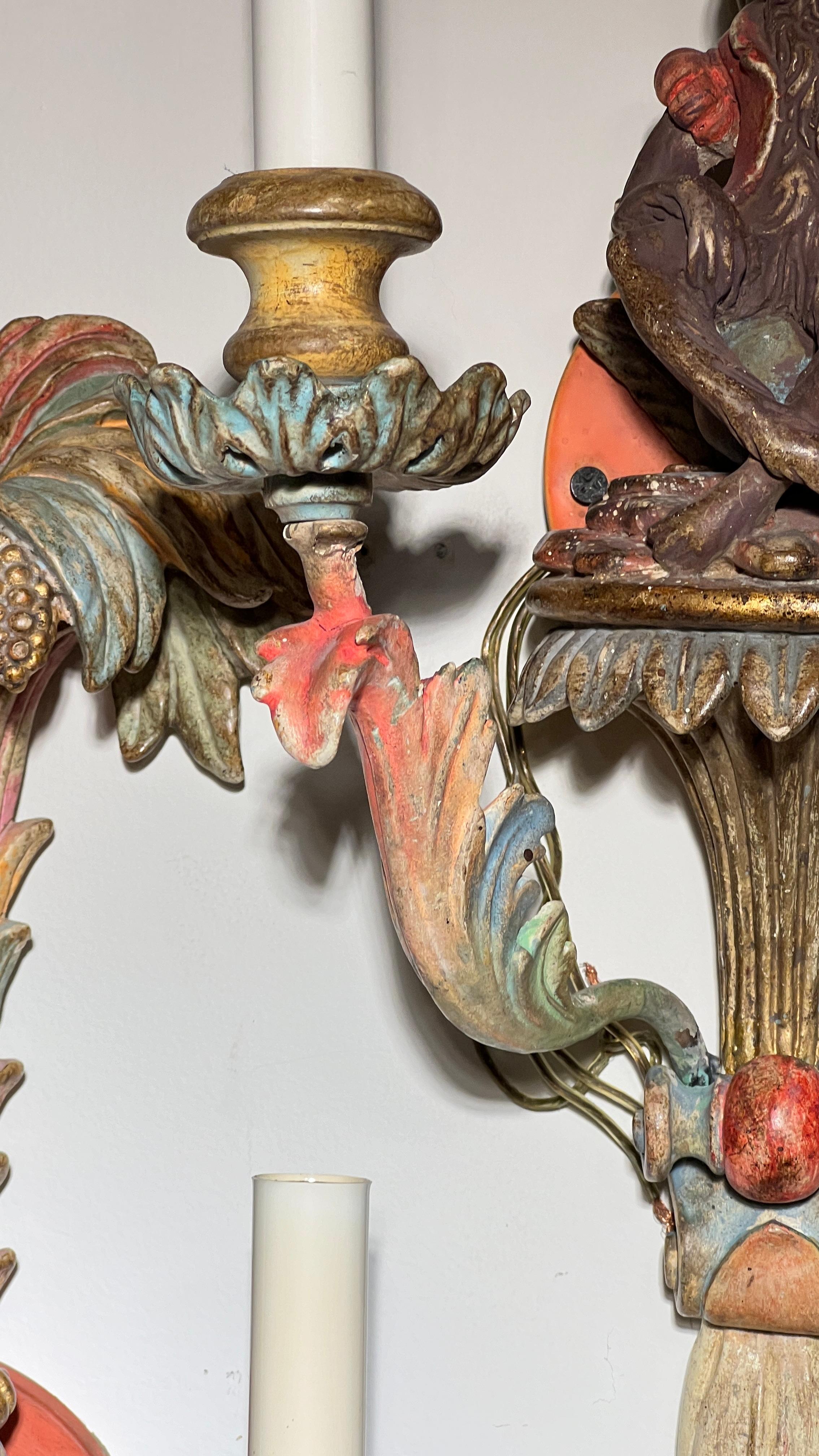 Pair of vintage wall lights in the 19th century Venetian style, carved from wood and depicting seated monkey below palm trees with drapery and tassel motifs and foliate shaped candle arms.  With two candelabra size sockets and wiring, ready for use.