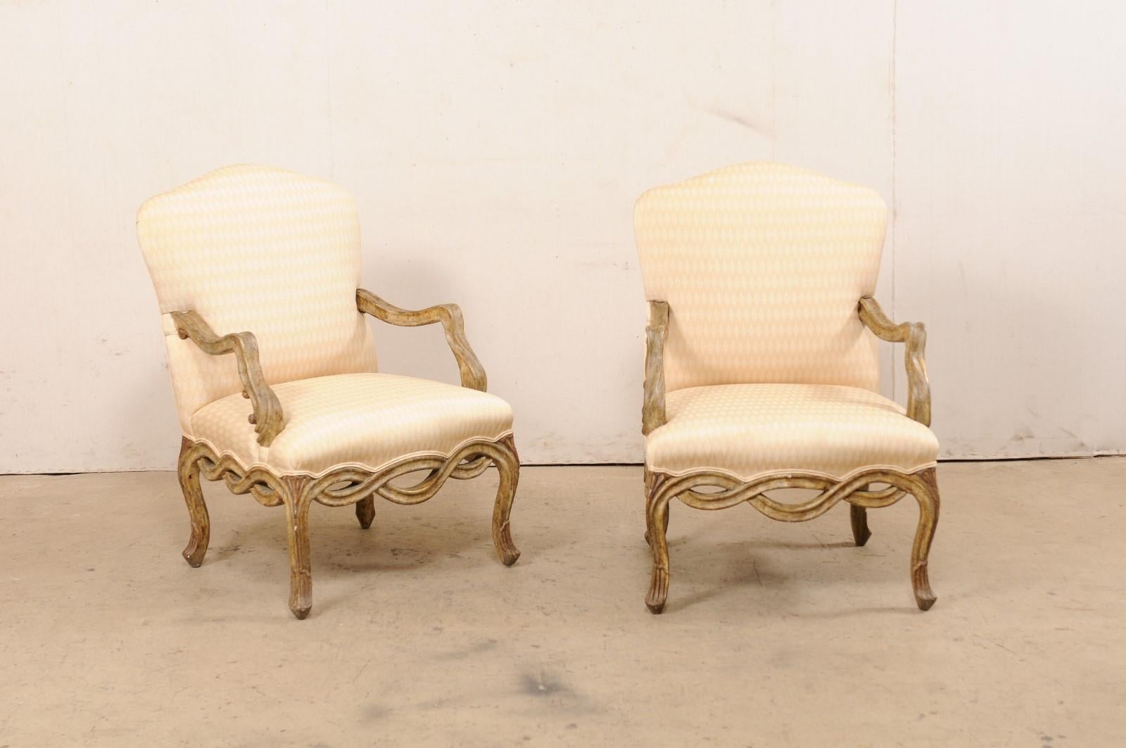 A vintage pair of American carved-wood and upholstered armchairs. These vintage chairs have been carved with Venetian-style influences, with beautifully carved-wood arms that have c-scroll accents, and the pierce-carved and intertwining ribbon that
