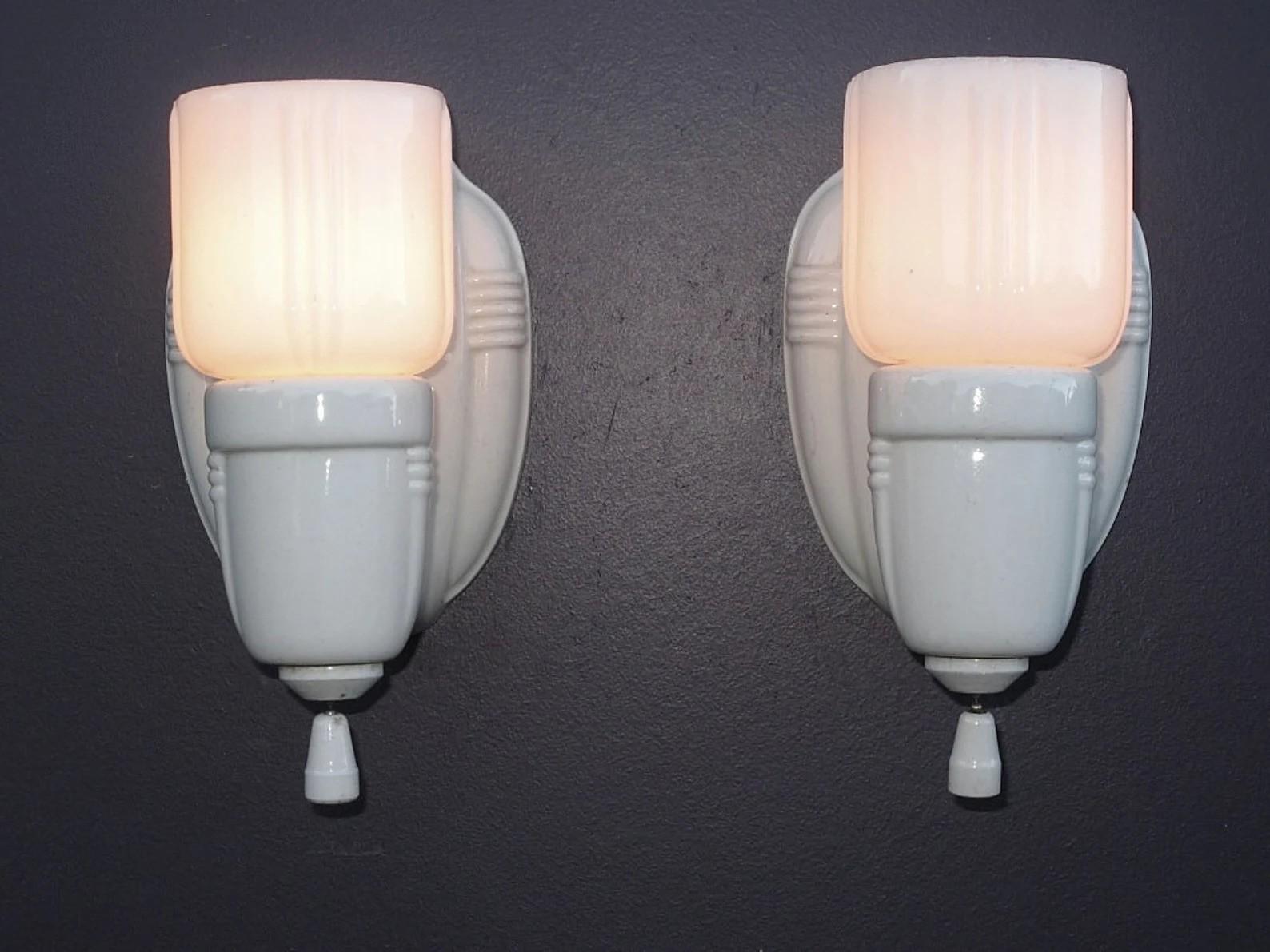 Priced and sold by the pair.
These vintage bathroom or vintage kitchen wall lighting sconces are classic 1920s -1930s decor. White porcelain lamps with period white shades. Clean lines with an Art Deco influence. Both porcelain and shades in