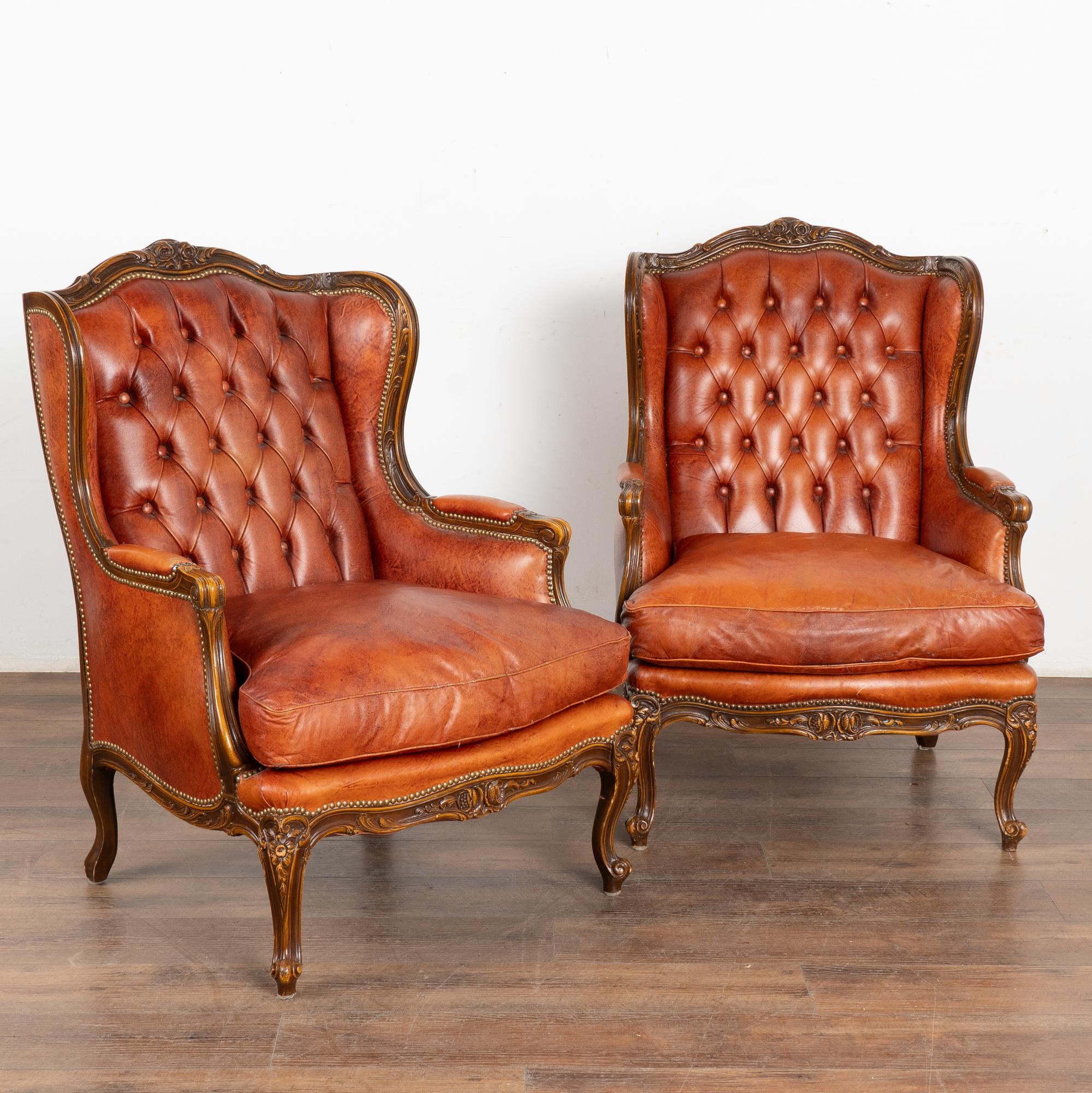 Pair, vintage brown leather Chesterfield wingback club chairs.
Wing sides, carved cabriolet feet, buttons and nail head trim in place. 
Vintage leather reflects typical age related wear including minor scratches, scuffs, stains, impressions,