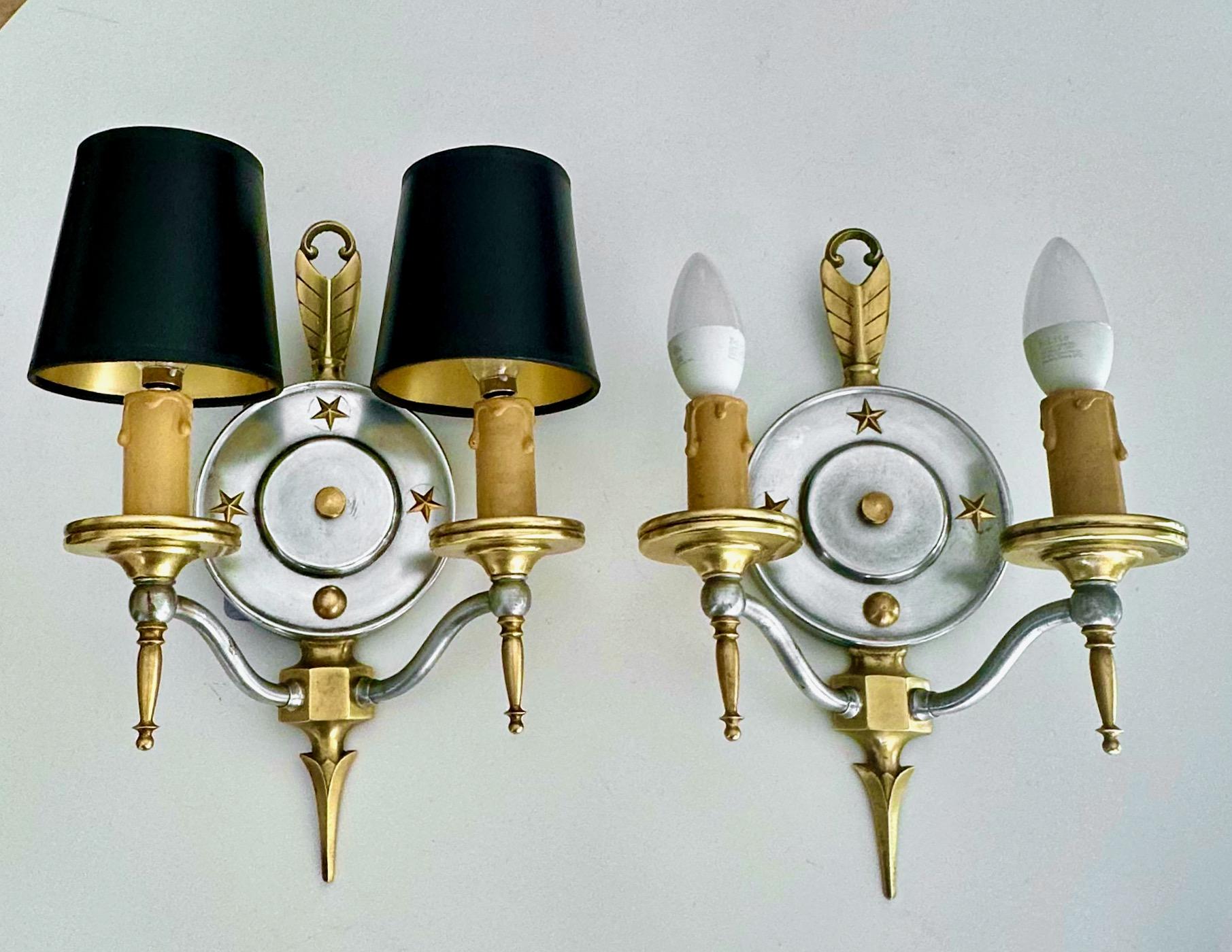 Paire d'appliques murales en laiton et acier A.I.C. Steele, de style Empire américain, à motif d'étoiles et de flèches. Chacune comprend 2 lampes avec des abat-jour noirs et dorés à clipser. Nouveau câblage pour l'installation aux États-Unis. 