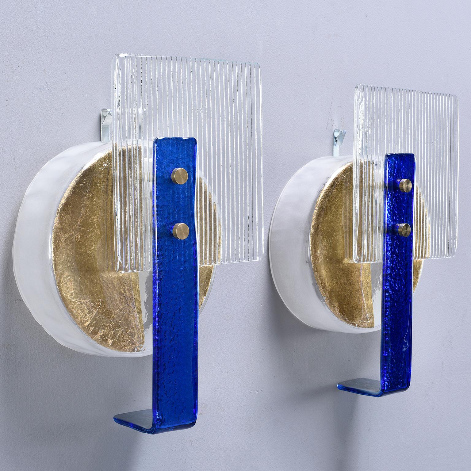 Pair of wall sconces made of vintage Murano glass elements, circa 2010. Clear ribbed glass squares with royal blue glass accents and gilded glass base. New wiring for US electrical standards. Unknown maker. Sold and priced as a pair.