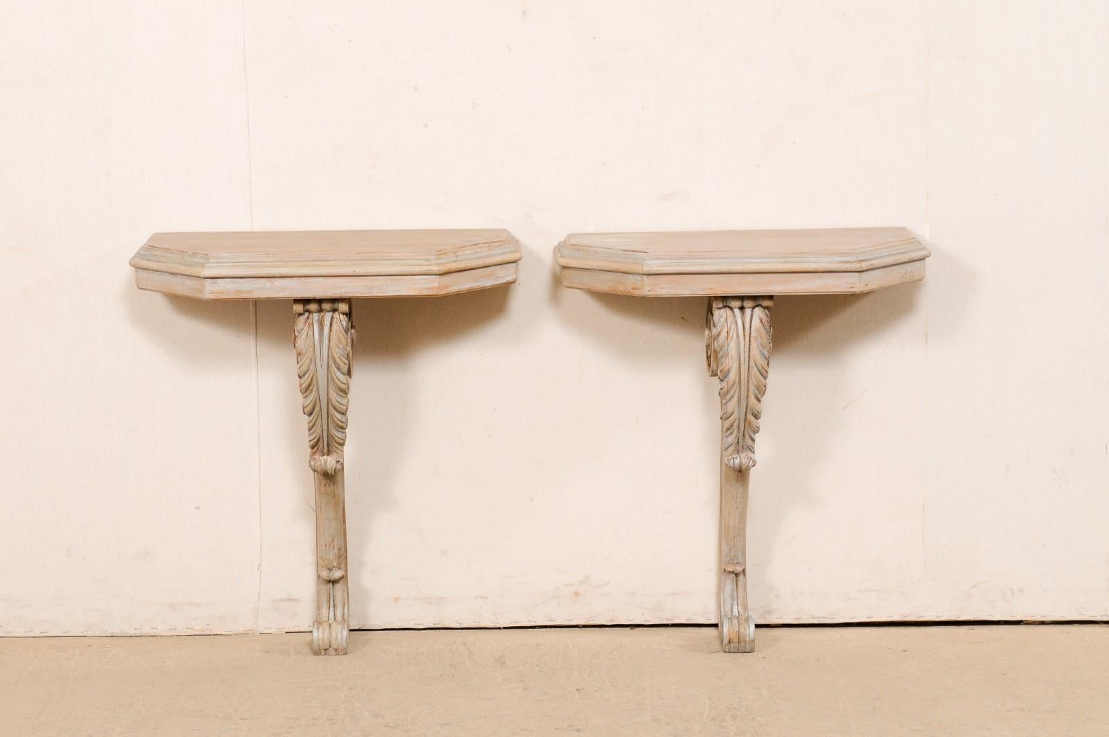 An American pair of carved-wood and painted wall mounted consoles from the mid 20th century. This vintage pair of console tables have been designed in French style, with demi-polygon shaped top, which is supported with a single leg/brace of carved