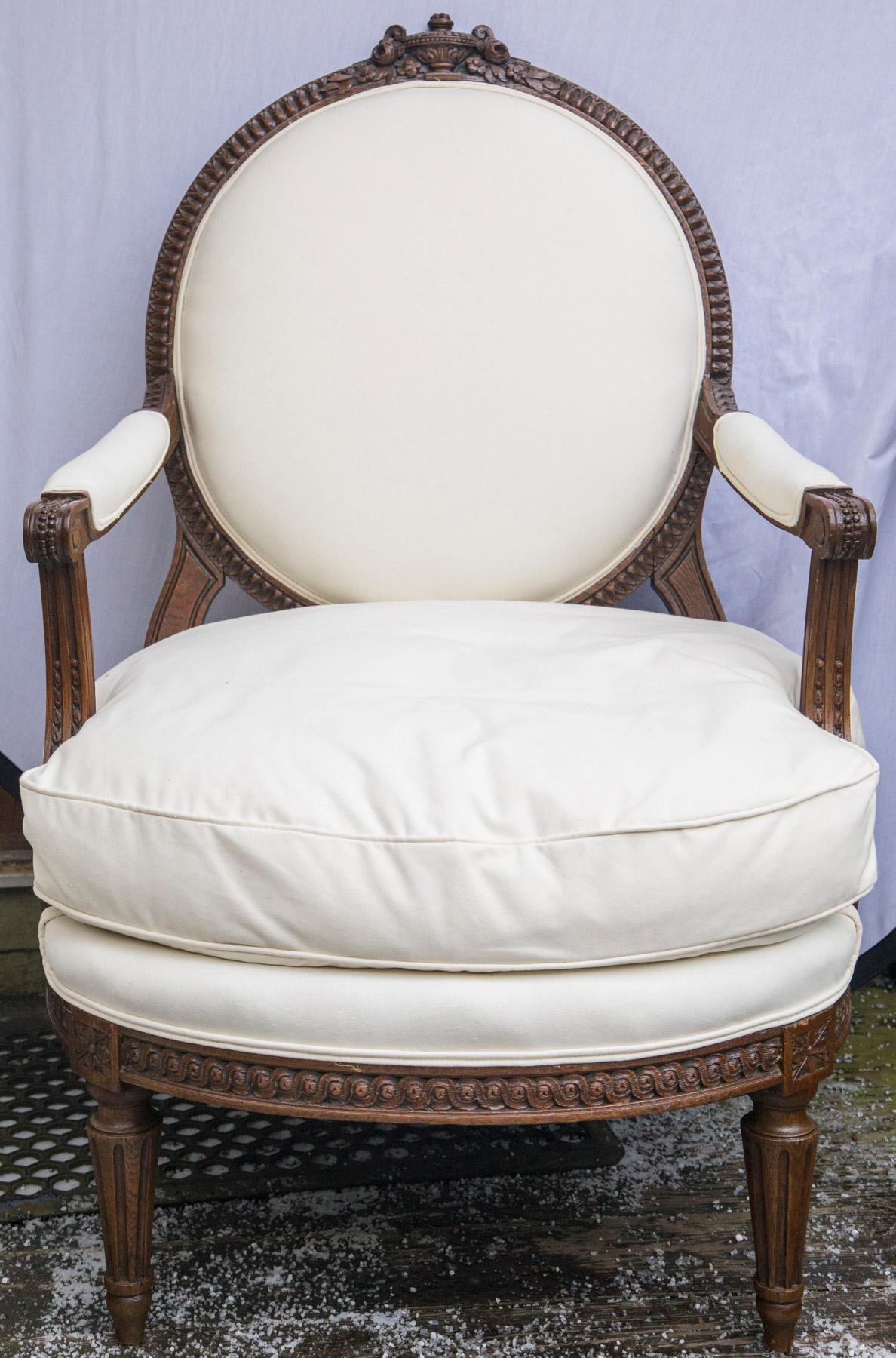 This pair of open arm chairs have been upholstered recently in white cotton muslin. 
Oval back with urn surrounded by flowers, centered
Carved arms, rails, and legs.
Legs of typical fluted, tapered Louis XVI style .
Very comfortable and ample.