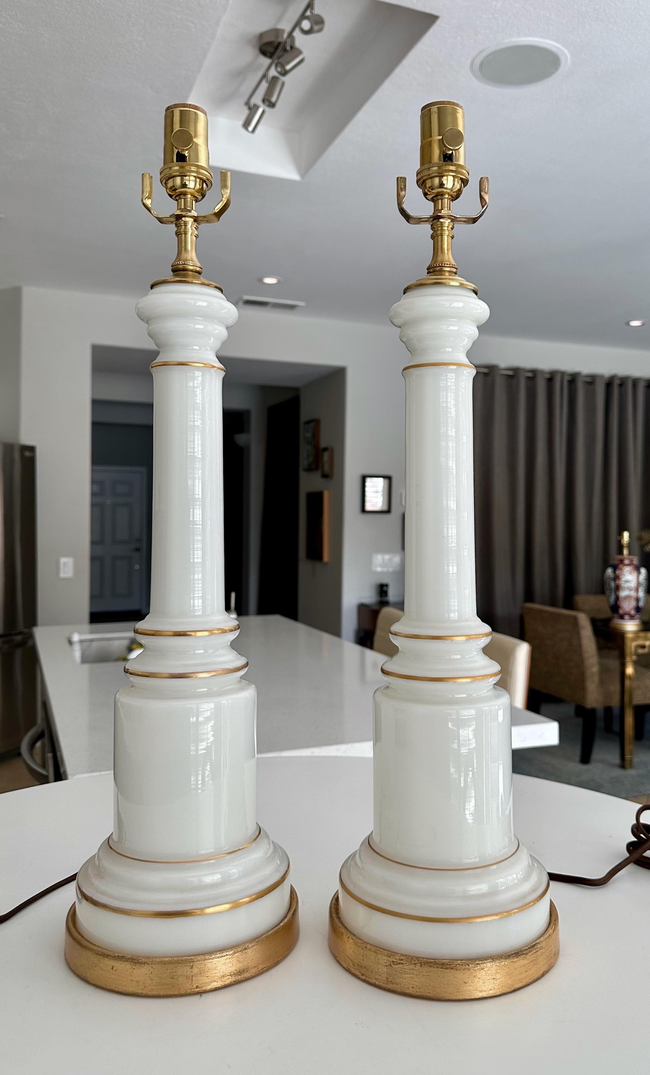Pair of table lamps by high end lamp manufacturer, Warren Kessler of New York. These lamps are made of white opaline glass with gilt pin striping, brass accents and gilt metal bases. These have all new US wiring, sockets and rayon cords. Each take a
