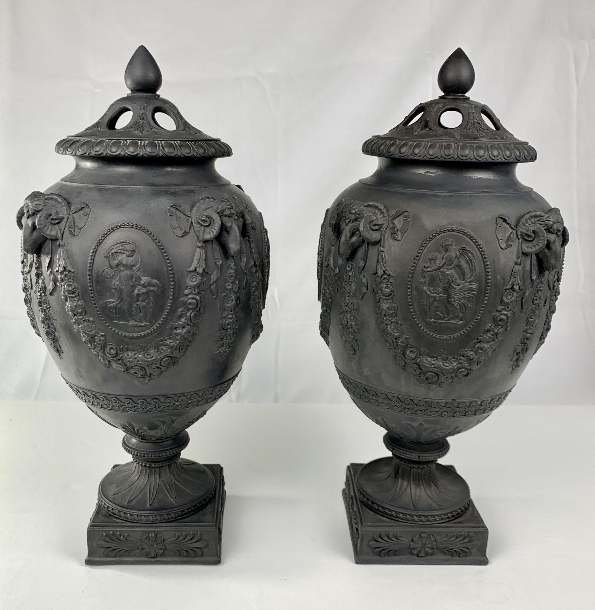 Wedgwood and Bentley made the design and molds for this pair of exquisite Wedgwood black basalt urns in the late 18th century. 
This lustrous pair was made circa 1840. 
Original antiquities from vases in the collections of 18th-century English