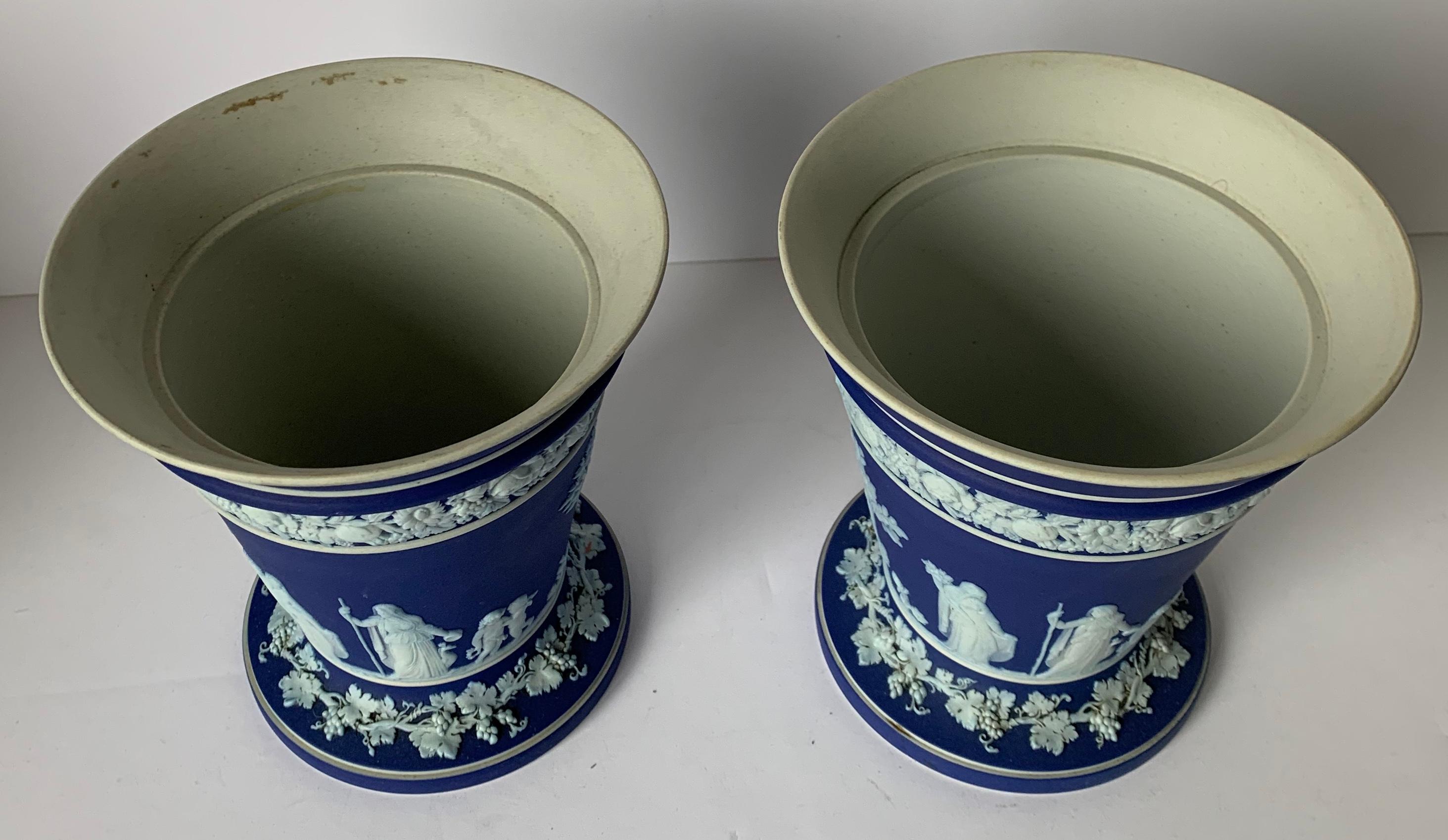 Pair of Wedgwood dark blue and white jasperware vases. Insides of vases have a shiny glazed finish. 6” tall x 5.5” across top x 4.5” across bottom. Stamped on the underside.