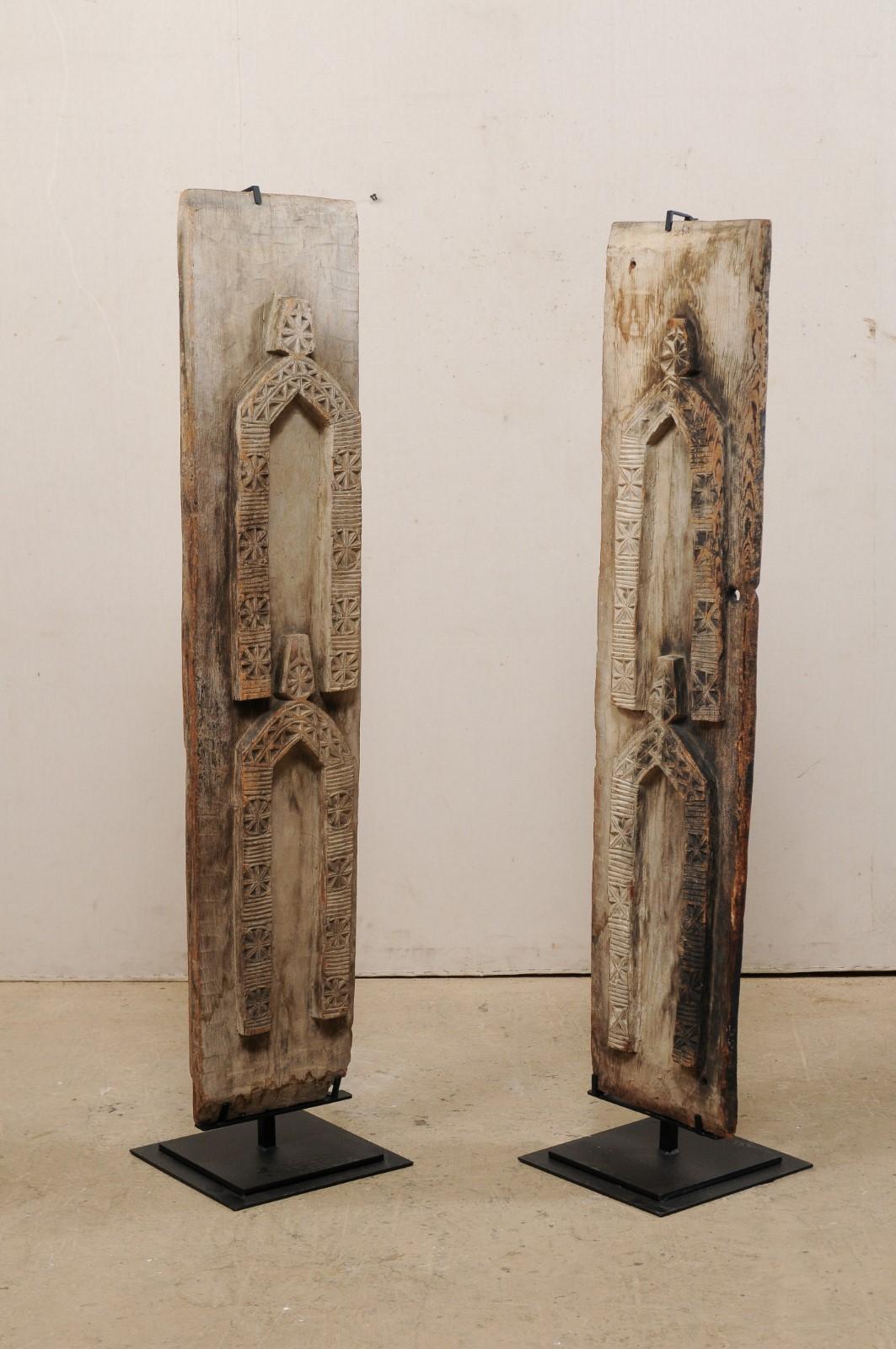 A pair of carved wood wall panels from West Africa, mounted on custom stands. This vintage pair of West African panels are each rectangular in shape with front sides which have been adorn in geometric hand-carvings in a human-shaped form. These