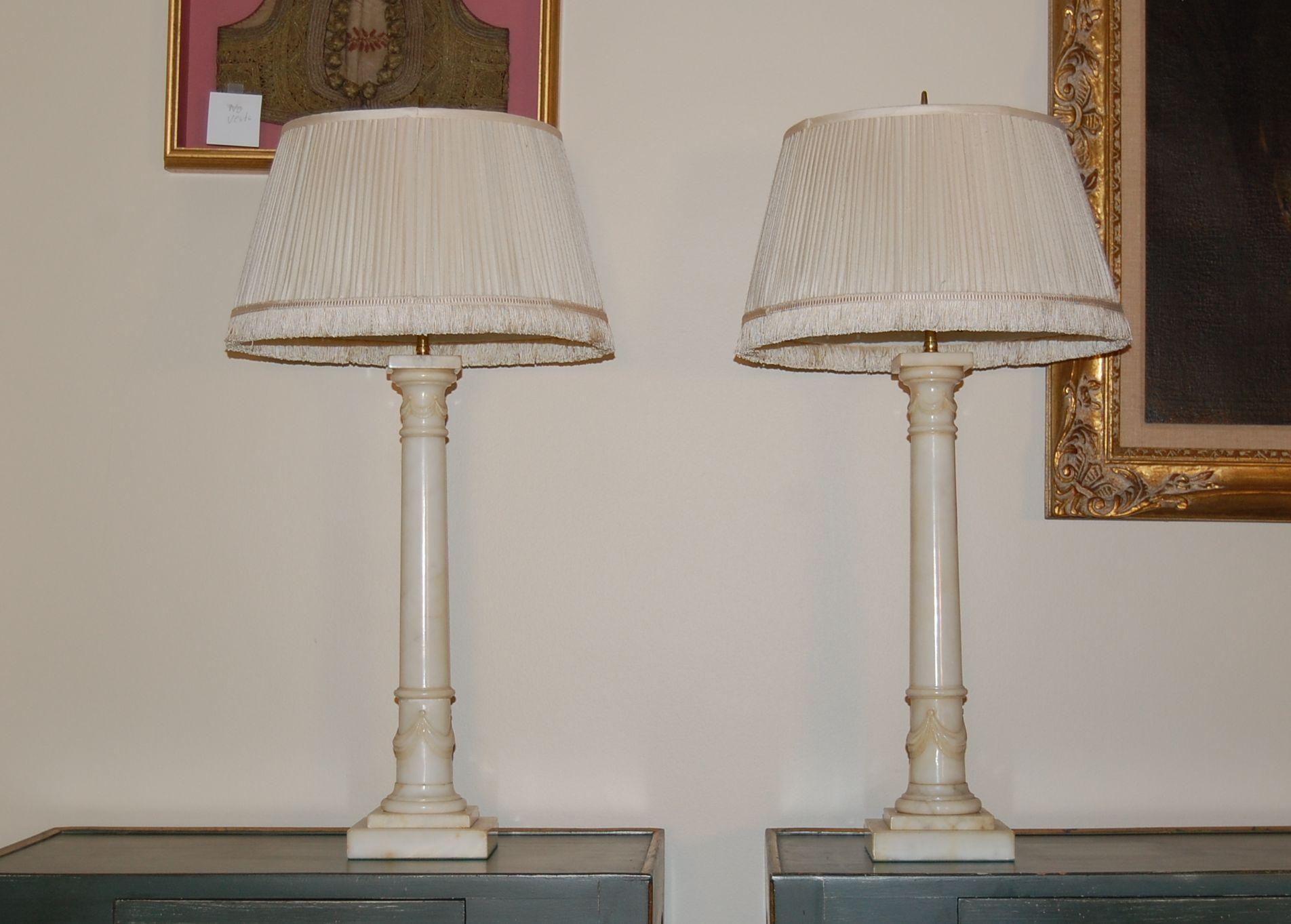A pair of carved white Italian Alabaster column lamps with draped swags top and bottom with square caps and stepped bases in very good overall condition.