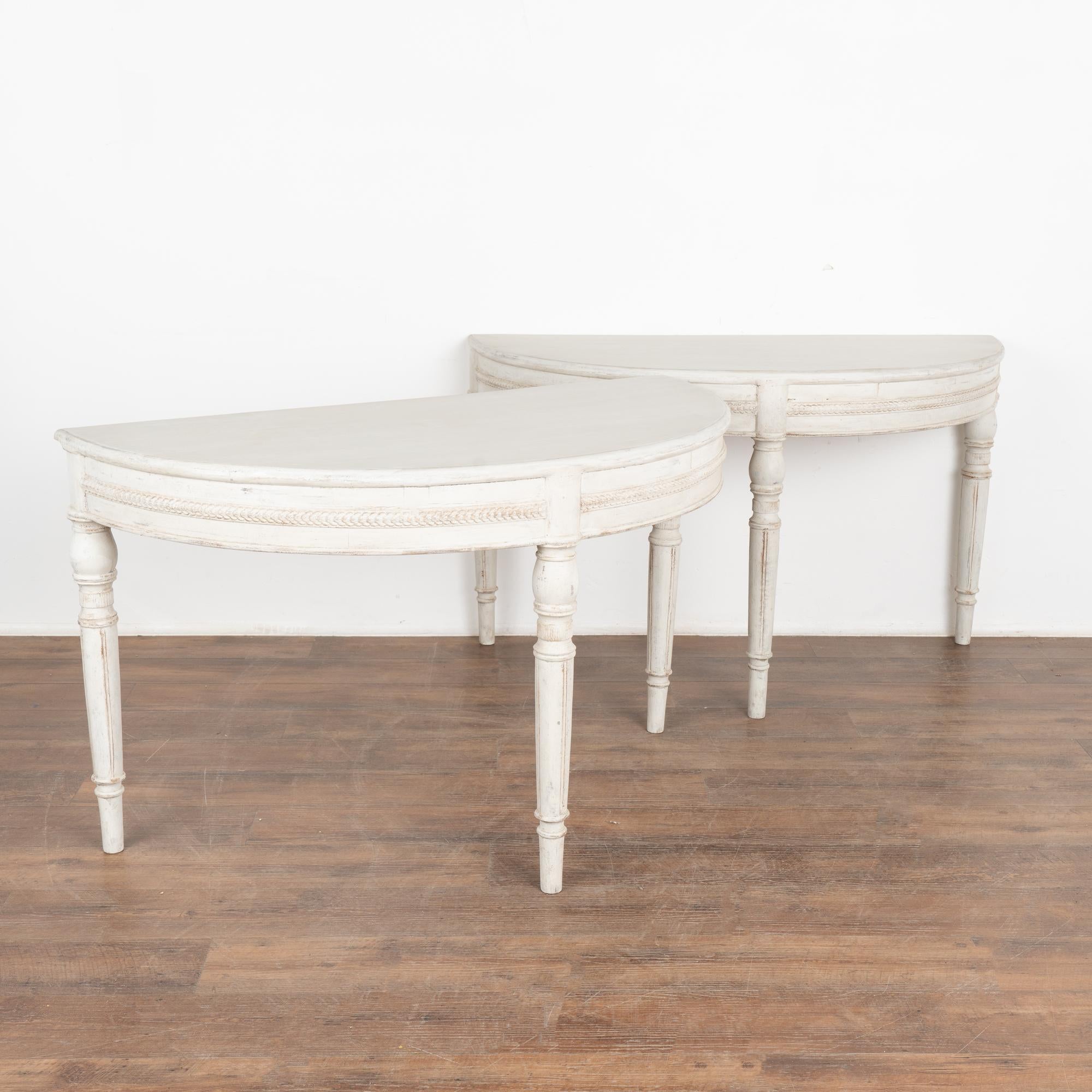Pair, Gustavian large demi-lune side tables or consoles. 
Turned legs and decorative carving along skirt add to the timeless appeal of these demilunes.
Newer professionally applied layered white painted finish, slightly distressed to fit age and