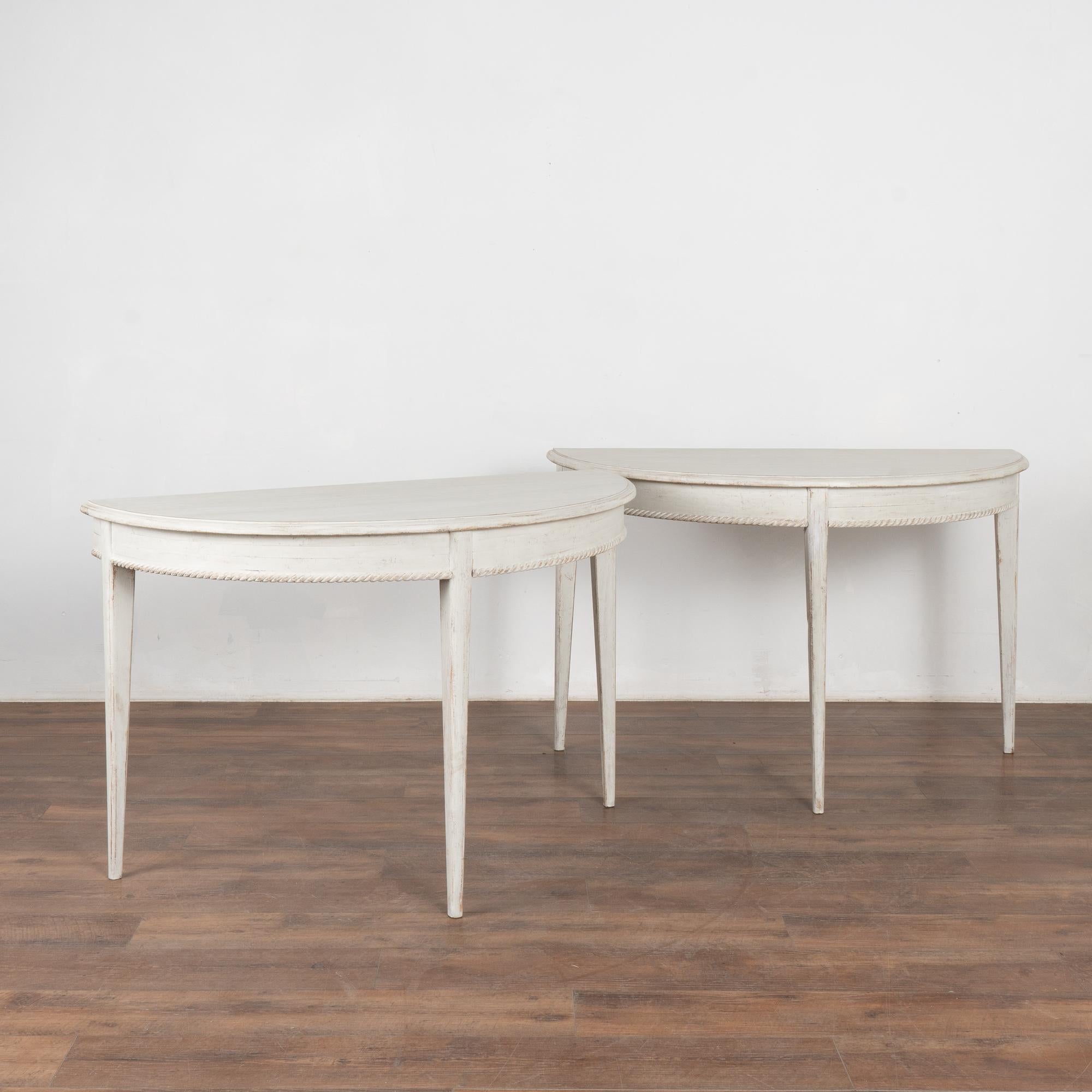 Pair, Gustavian demi-lune side tables or consoles. 
Gently tapered fluted legs with simple carved braid motif accenting the lower skirt. 
Newer professionally applied layered white painted finish, slightly distressed to fit age and grace of the