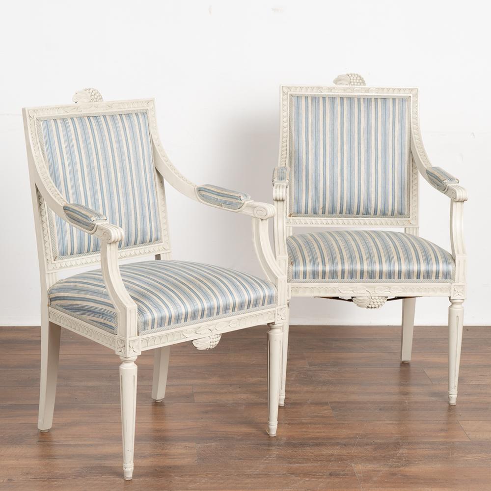 Pair, Swedish white painted armchairs with carved details along edges, top of back and bottom of seat.
The white painted finish is typical of the 1900's era in Sweden.
The original blue and white fabric accent the Swedish Gustavian feel of these