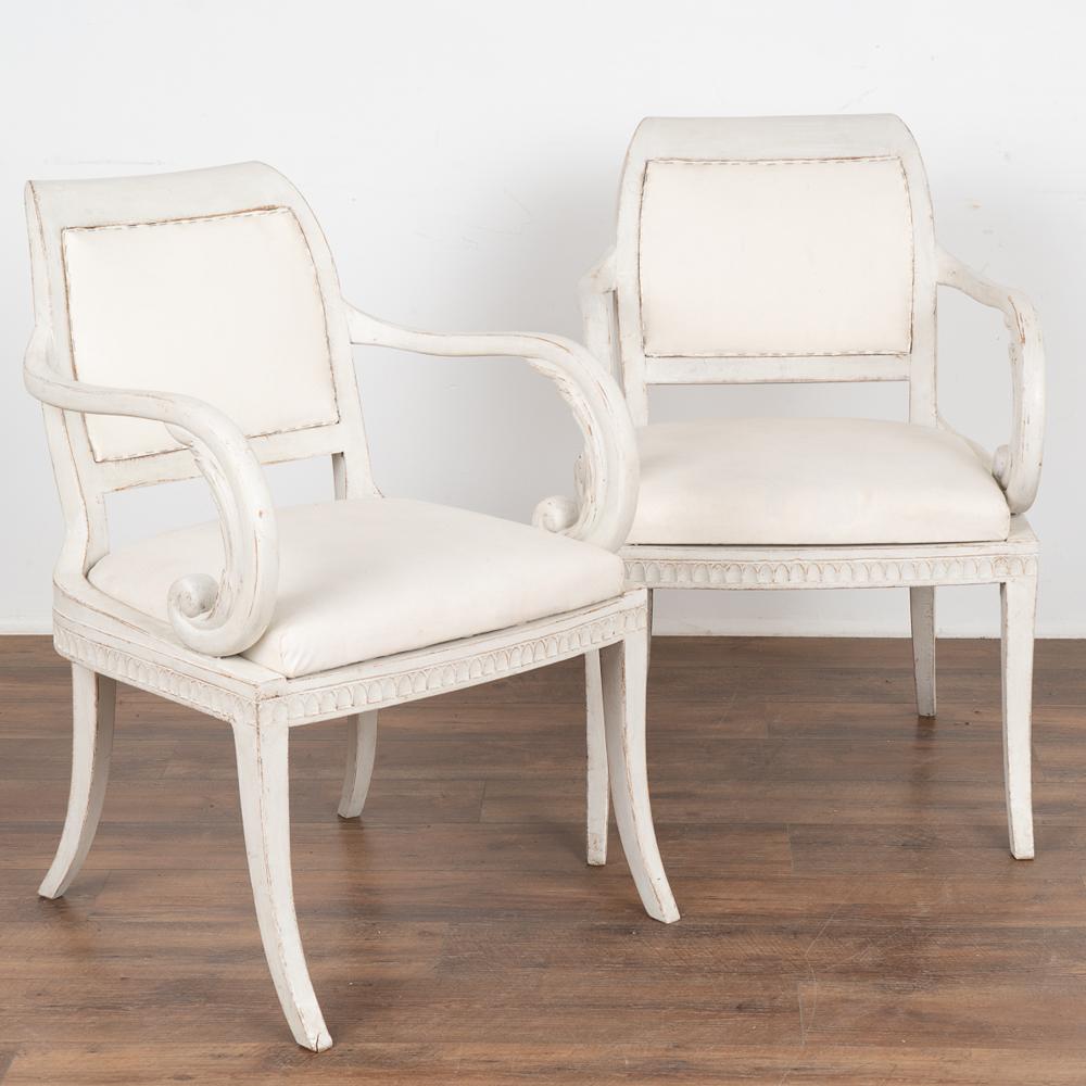 Pair, attractive Swedish country gustavian arm chairs with gracefully curved arms and legs.
The newer white painted finish is lightly distressed fitting the age of these lovely side chairs. 
Restored, stable ready for use. Any signs of wear