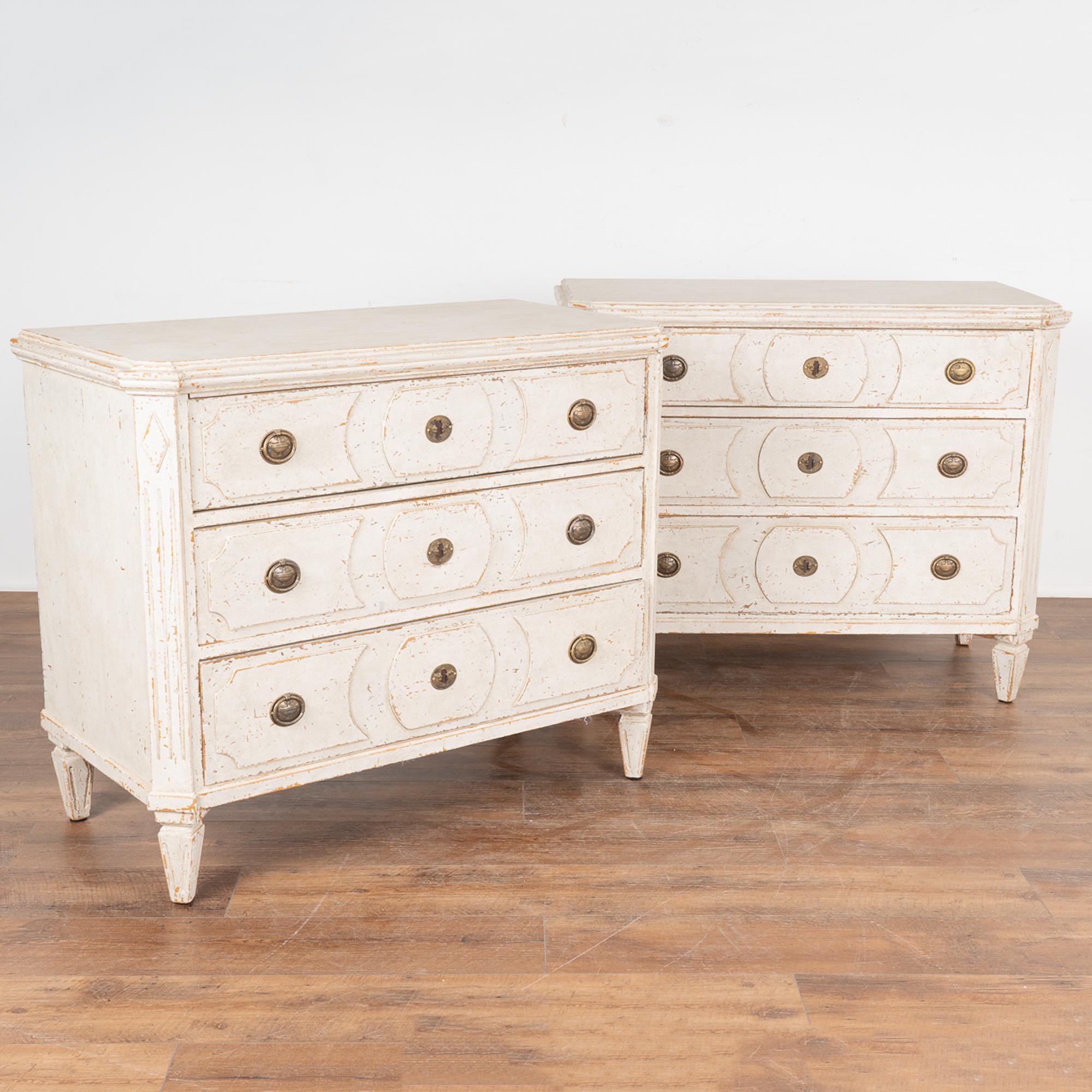 A pair of decorative Gustavian pine chest of drawers painted in shades of white, fitting their Swedish origin.
Canted fluted side posts with upper carved diamond medallion, raised carved panels along the three drawers, all setting on four tapered